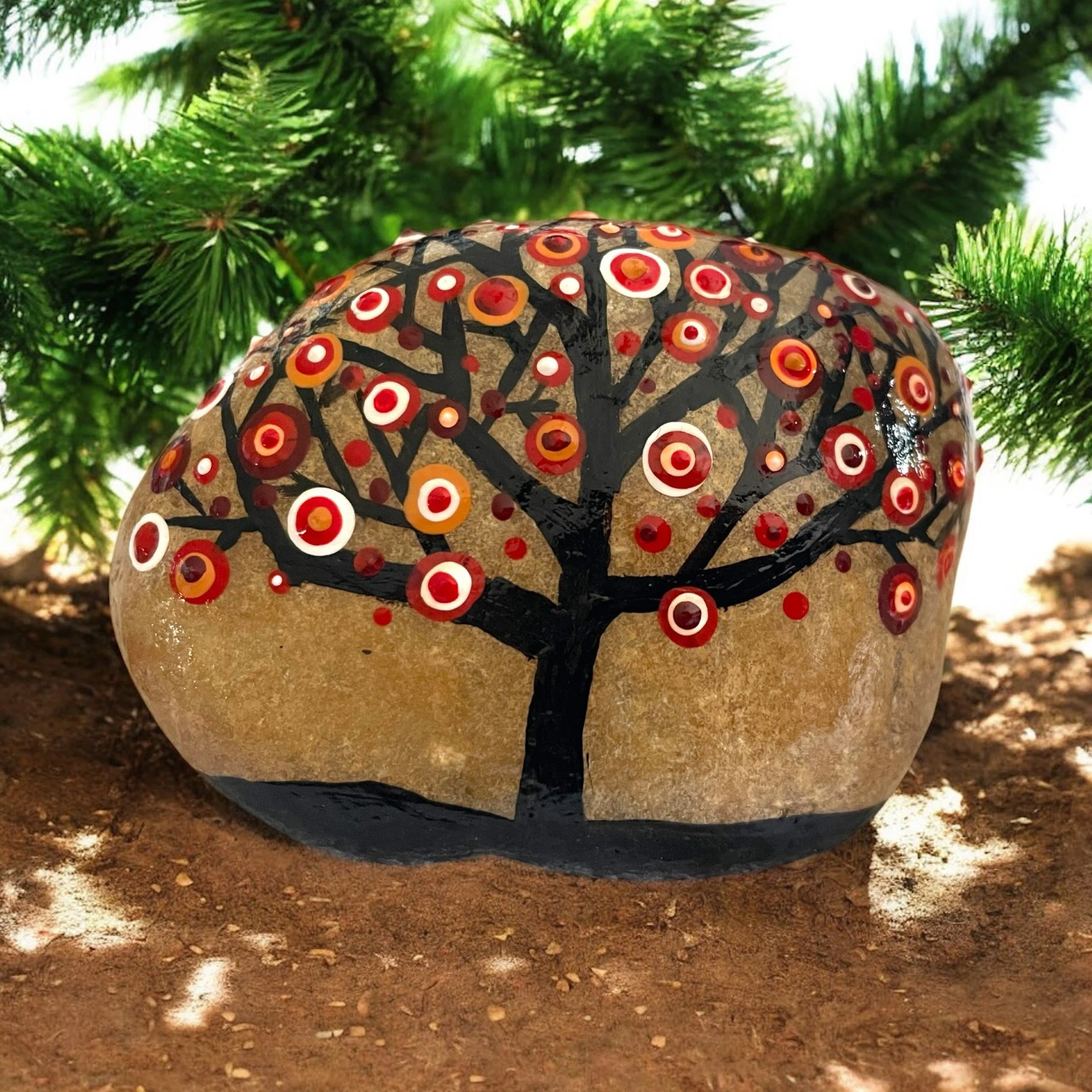 Rock painted with a black tree featuring branching limbs adorned with circular dot patterns in shades of red and white, resembling abstract blossoms.