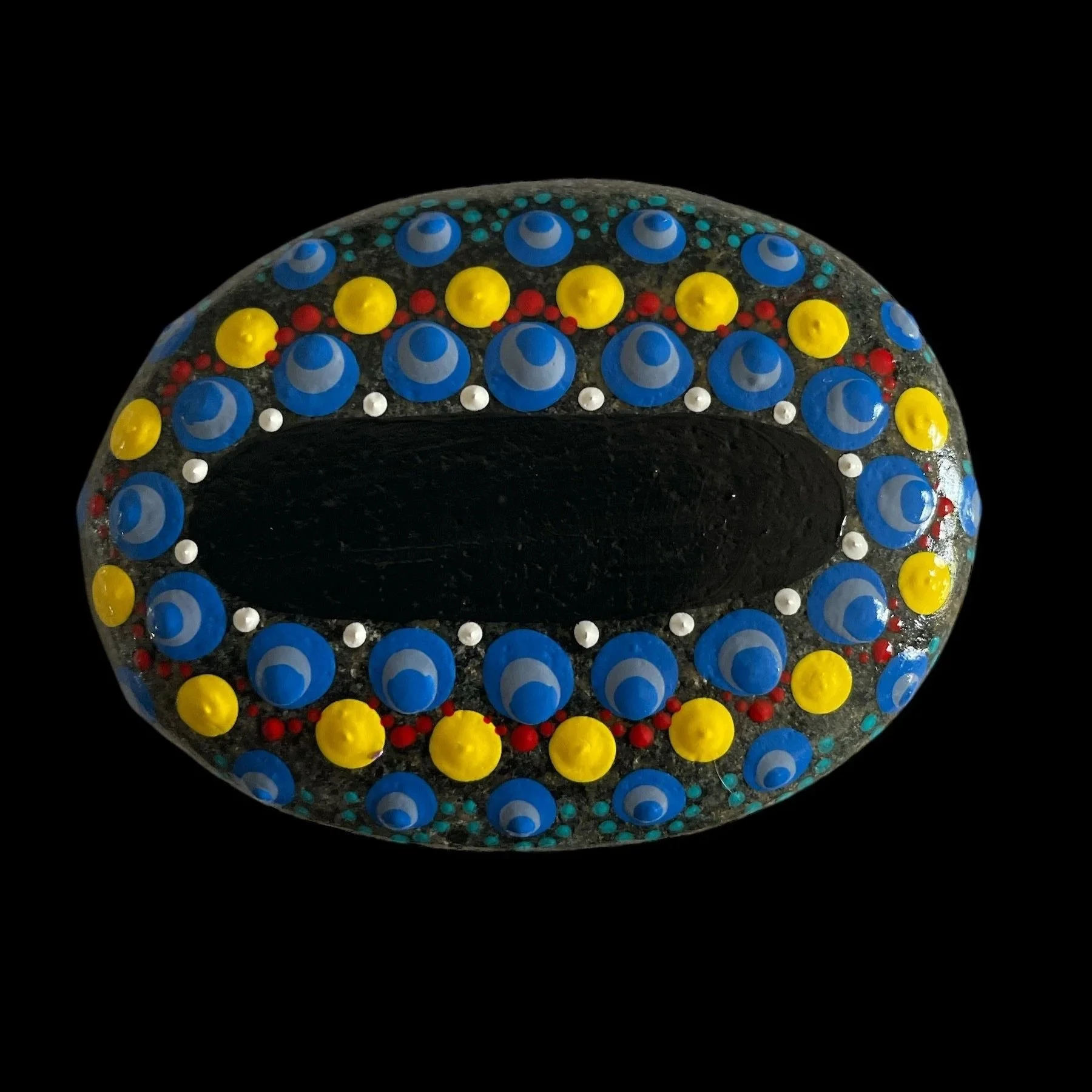 Oval rock with intricate dot painting in concentric circles of yellow, red, blue, and white on black background