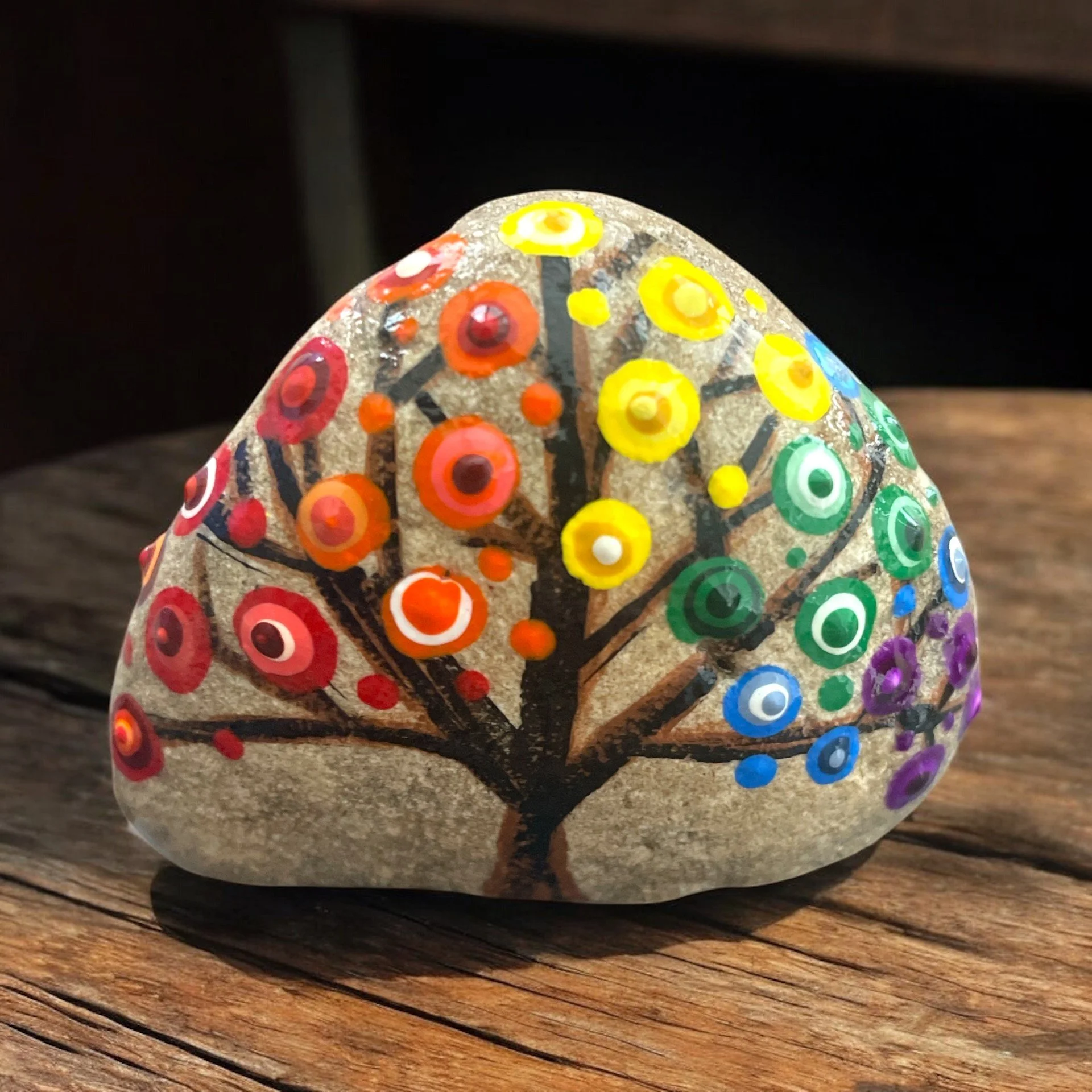 A brown tree featuring branching limbs adorned with circular dot patterns in shades of rainbow colors, resembling abstract blossoms.
