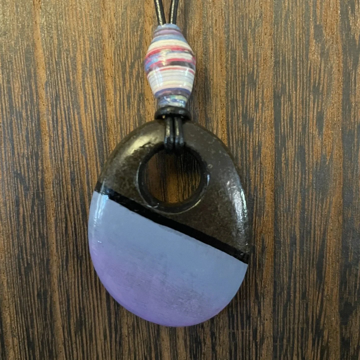 This one-of-a-kind pendant necklace features a natural stone with a hand-drilled hole, transformed into wearable art through the intricate dot painting technique.