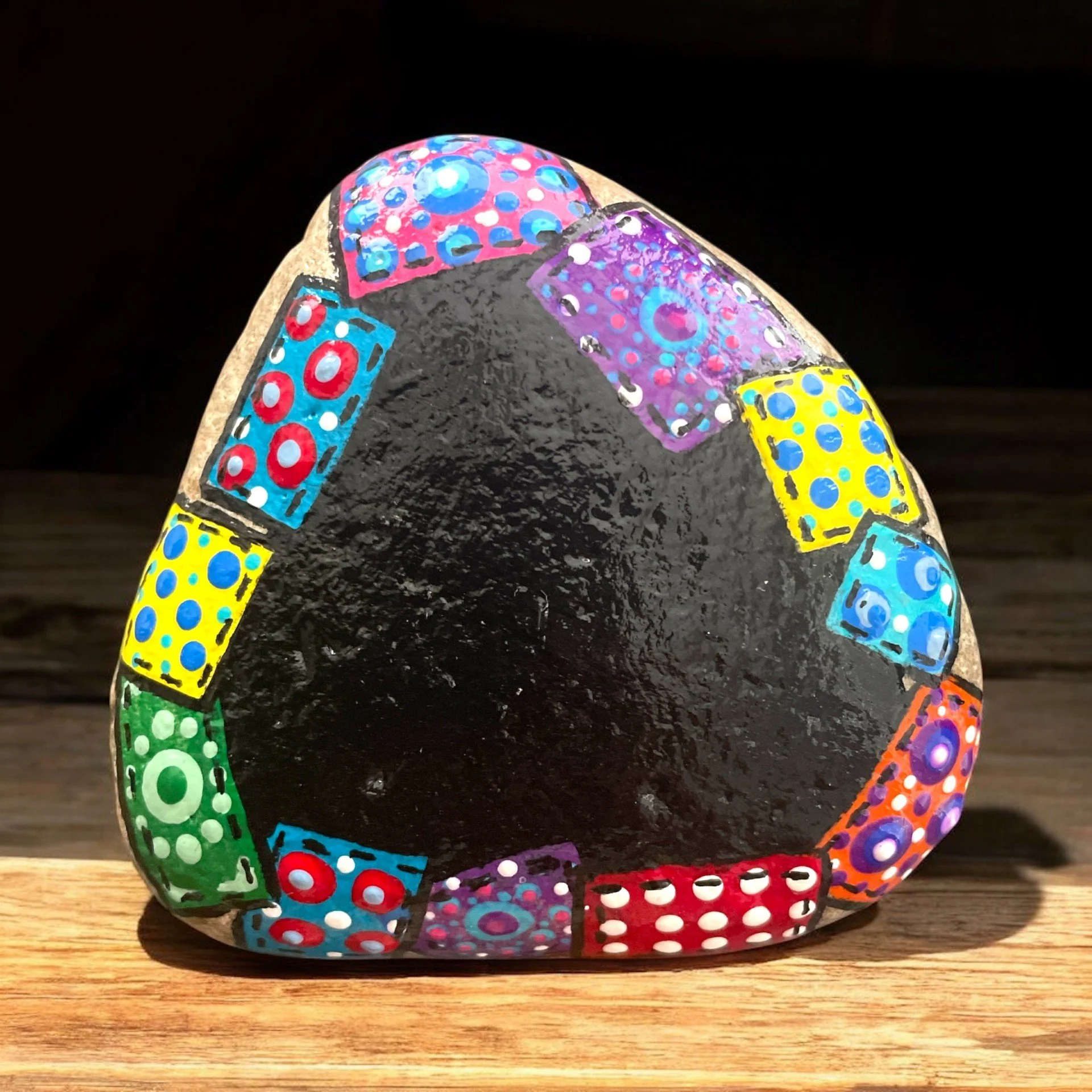Painted rock of a black chalkboard with a colorful, patterned quilt patches, surrounded by succulents.