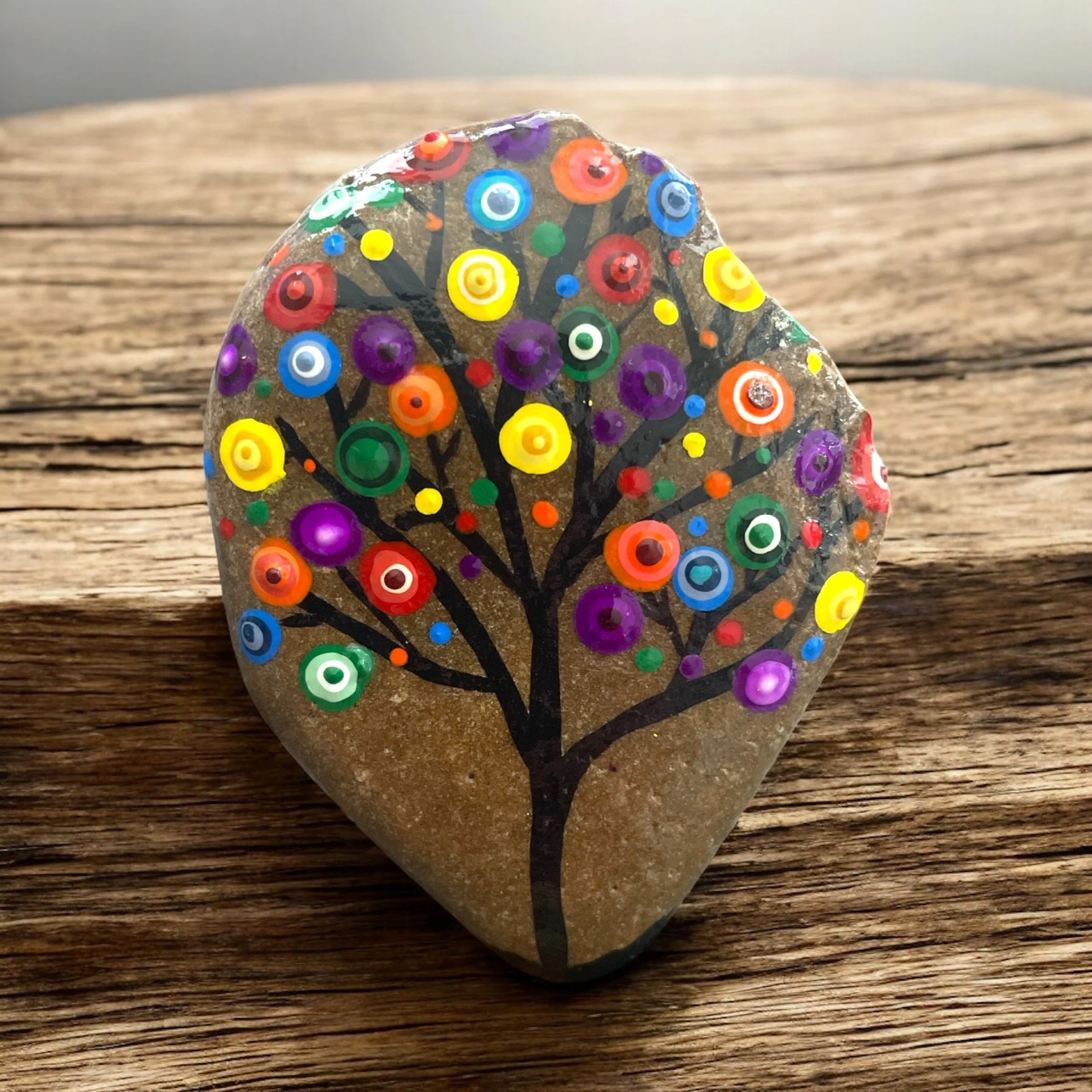 A black tree featuring branching limbs adorned with circular dot patterns in shades of rainbow colors, resembling abstract blossoms.