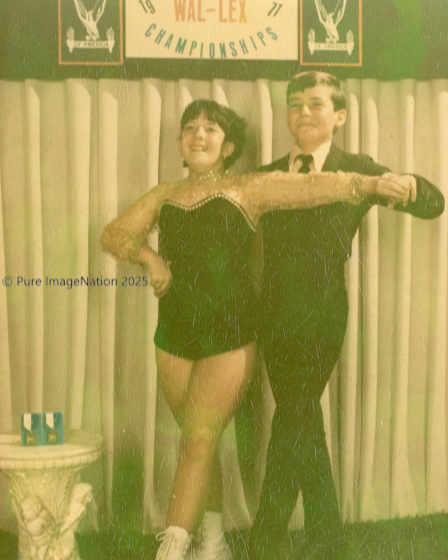 A man and woman stand in a dance hold in roller skates in a formal costumes