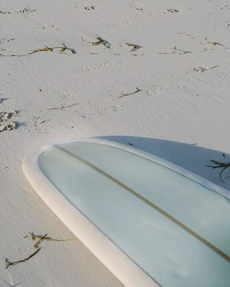 A surfboard lying on white sandy beach with scattered seaweed.