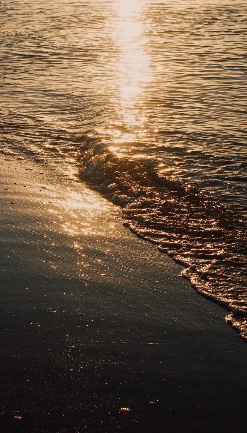 Sunset over the ocean with gentle waves reflecting golden light.