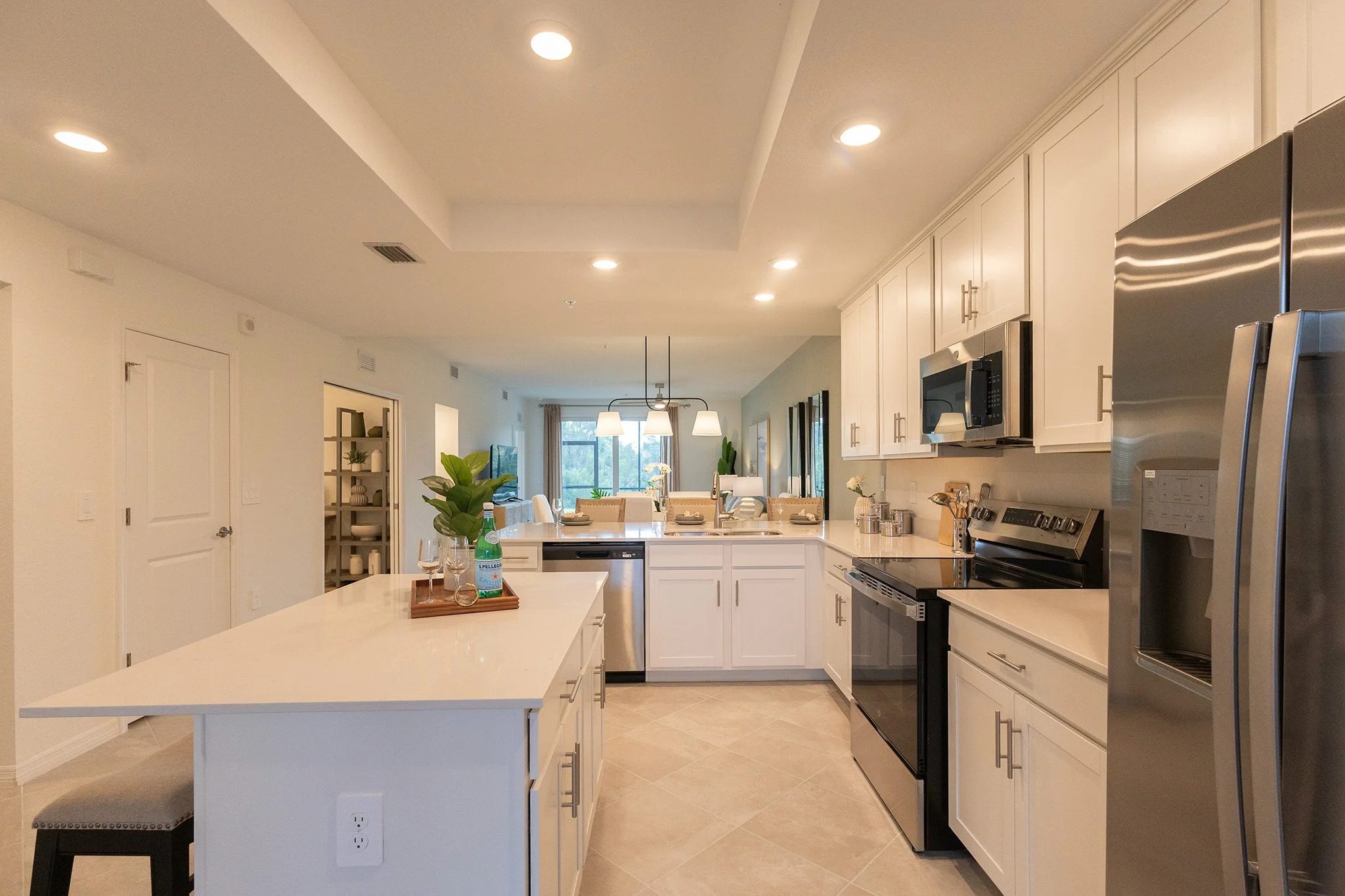 Modern kitchen with white cabinets, stainless steel appliances, a large island, and a dining area with hanging lights, windows, and decor.