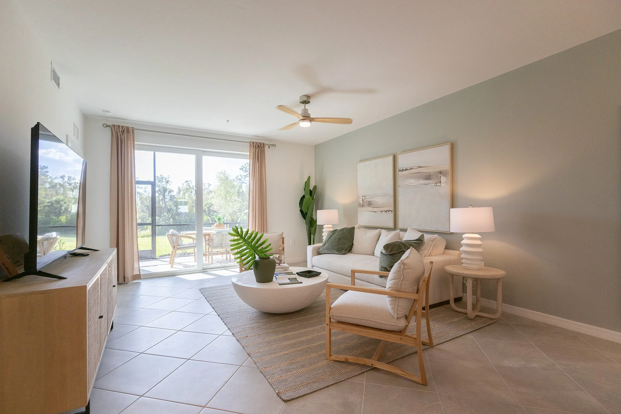 Living room with a white sofa, wooden armchair, white coffee table with a plant, and a large sliding glass door leading to an outdoor patio