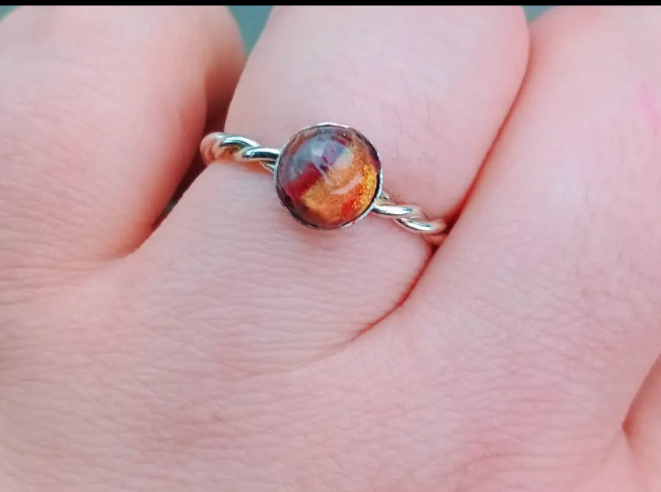 A close-up of a hand wearing a silver ring with a dark, round stone that has red, orange, and black hues.