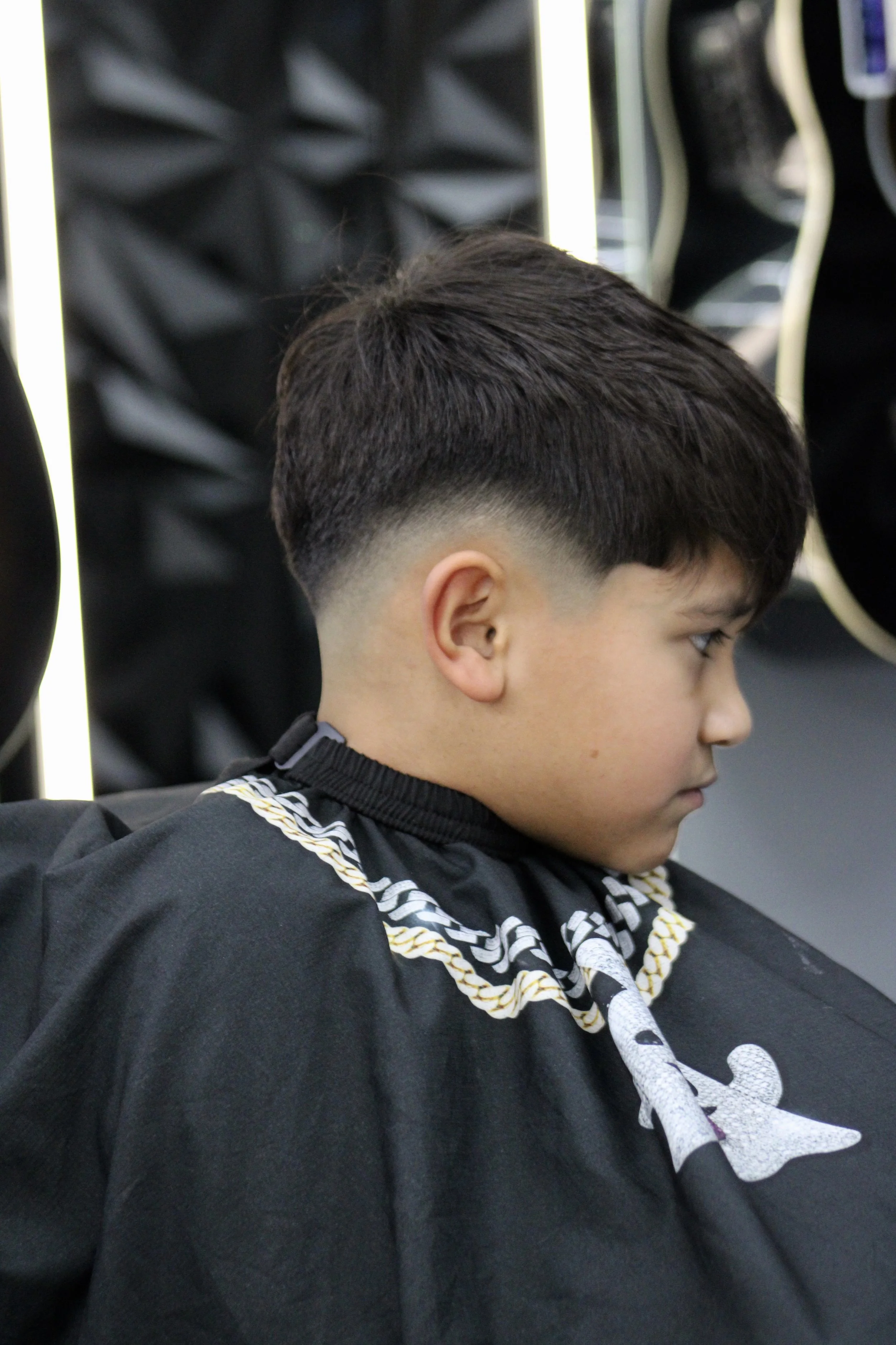 A young boy with a fresh fade haircut, sitting in a barbershop.