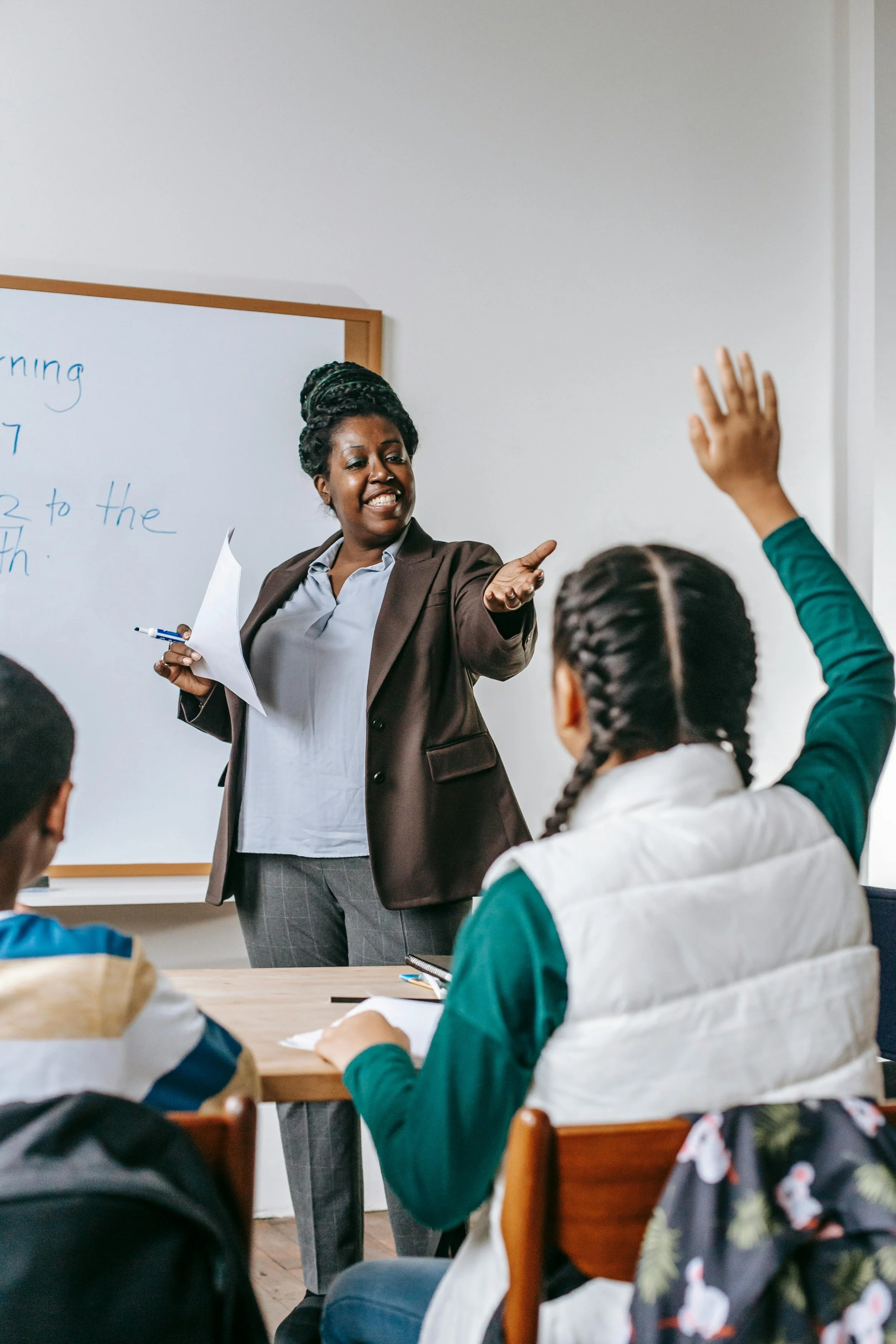 Teacher is pointing at a student with her hand raised asking a question.