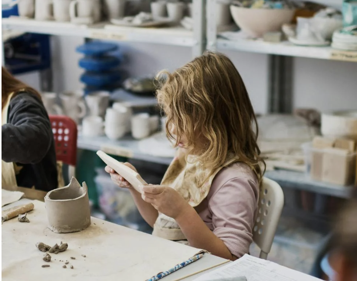 Girl looking at a clay tile while she is building a pinch pot