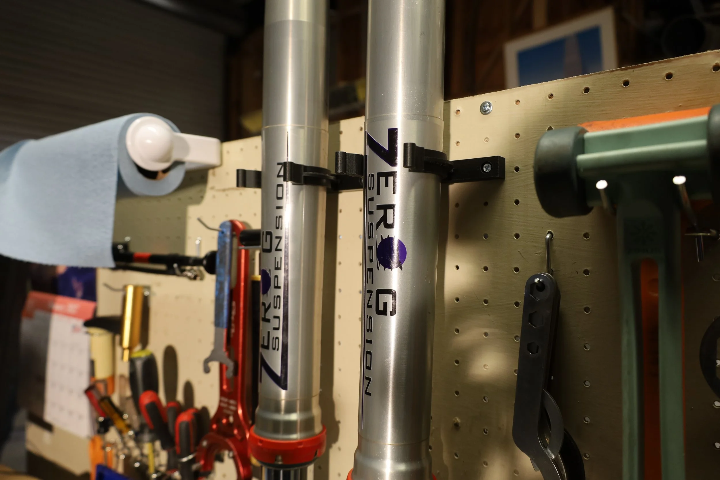 Close-up of metal stunt motocross suspension forks mounted on a pegboard with other tools.