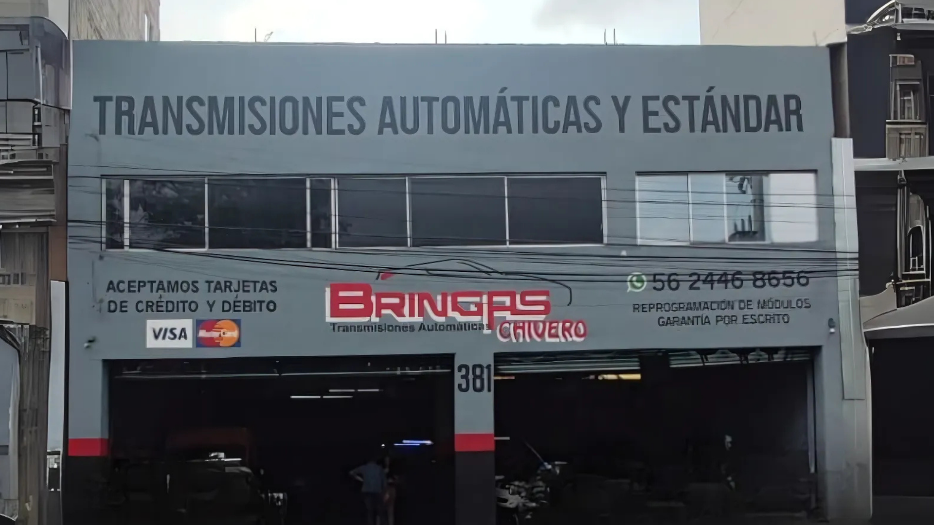 Fachada de taller mecánico con anuncio de transmisiones automáticas y servicios de pago con tarjetas de crédito y débito, incluyendo la marca Visa.