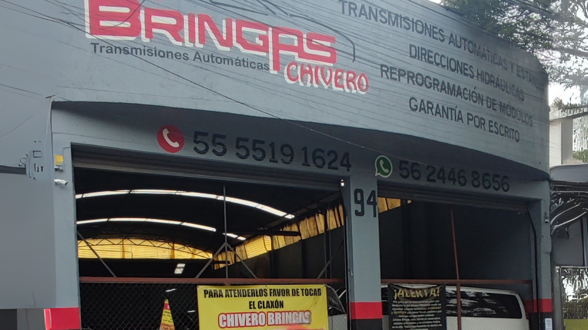 Fachada de un taller automotriz llamado Chivero Brings, que ofrece servicios como transmisión automática, hidráulicas, reprogramación de módulos y garantía por escrito, con números de contacto y un cartel en la entrada que indica atención para el toq