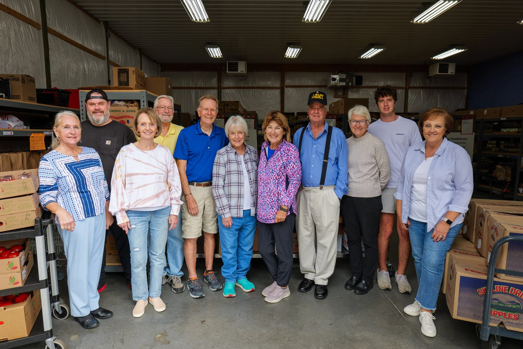 Group of fifteen people standing inside a warehouse with shelves of supplies and boxes around them.