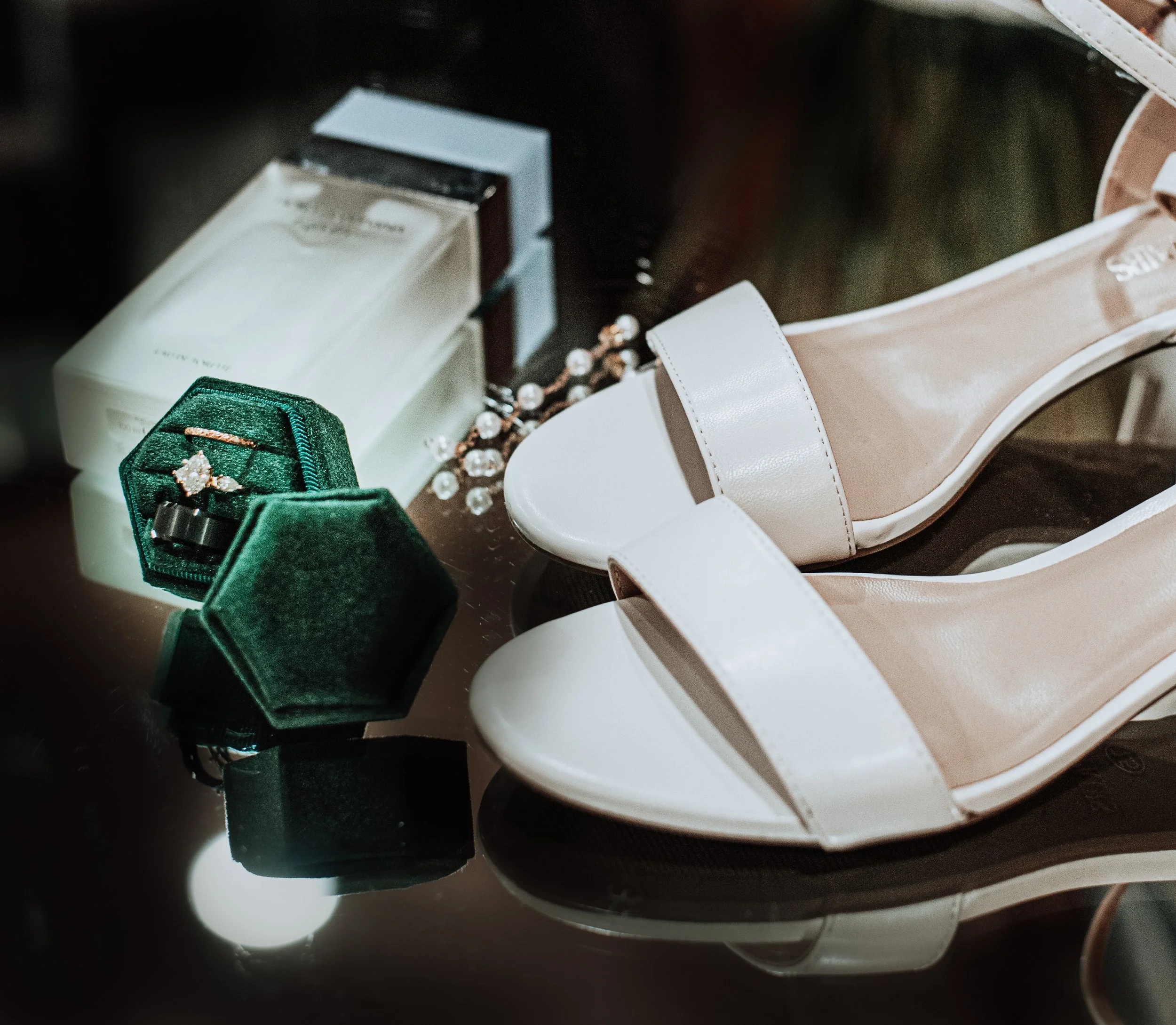 Bride shoes staged for photo emerald green ring box with engagement ring wedding band for bride and groom glass bottle of perfume glass pearl dangling earrings