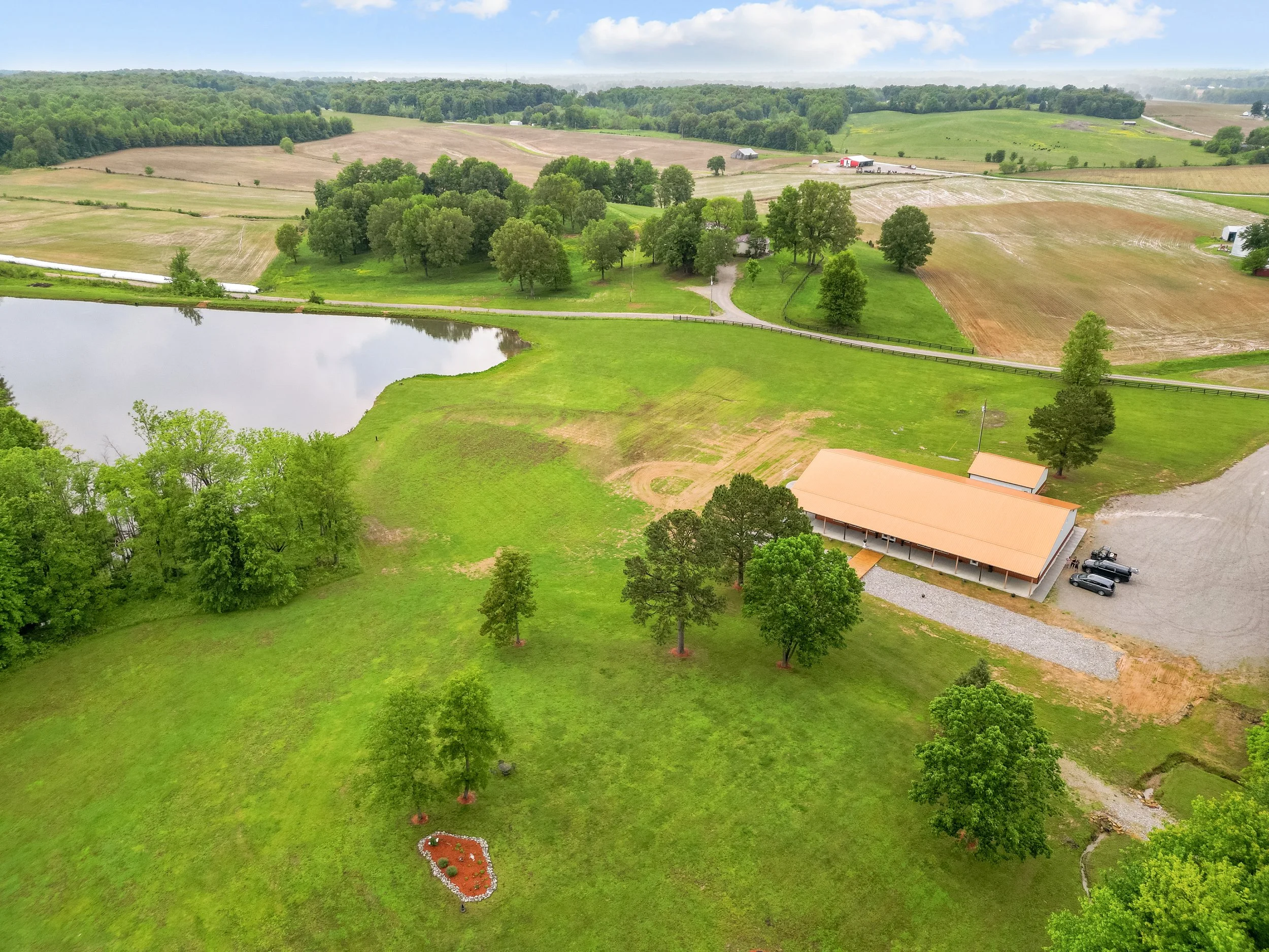 Owensboro Kentucky wedding venue elegant copper roof white building lake side lake view black fencing mature trees green grass rock landscaping flower garden parking area wooden bridge engagement wedding events