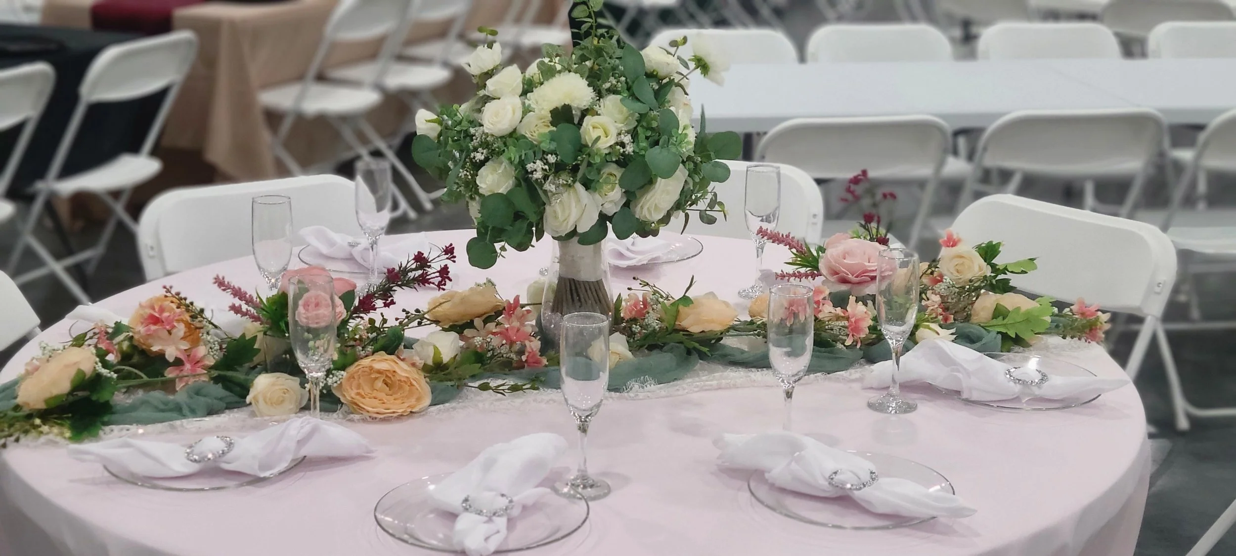 Owensboro Kentucky wedding venue guest table set up white table cloth green table runner greenery and floral runners elaborate floral centerpiece wine glass glass plates white napkin wrapped in diamond rings elegant formal fancy  bouquet