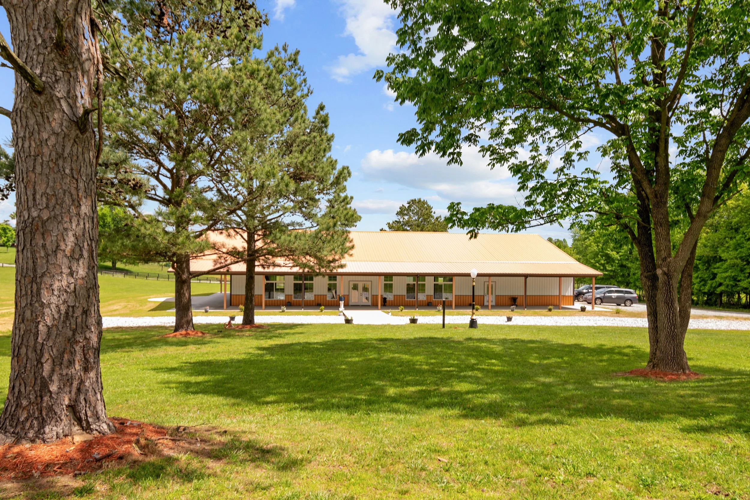 Owensboro Kentucky privately owned wedding venue large windows and doors glass panes large covered porch around building parking lot mature trees green grass rock landscaping copper roof unique flower pots in full bloom fencing  scenic views