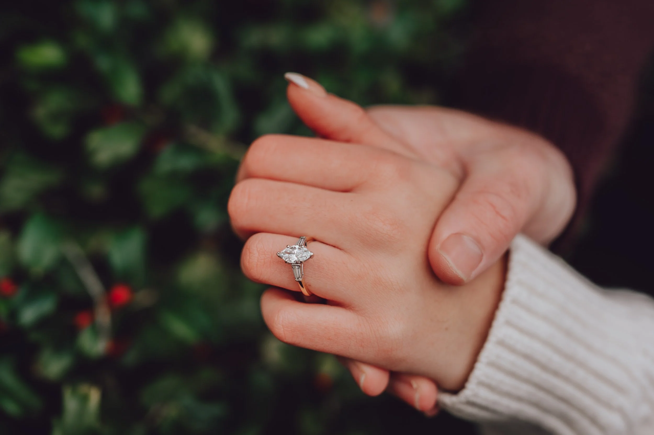 holding hands wearing white sweater and gold ring with diamond shaped diamond engagement photo capturing the moments