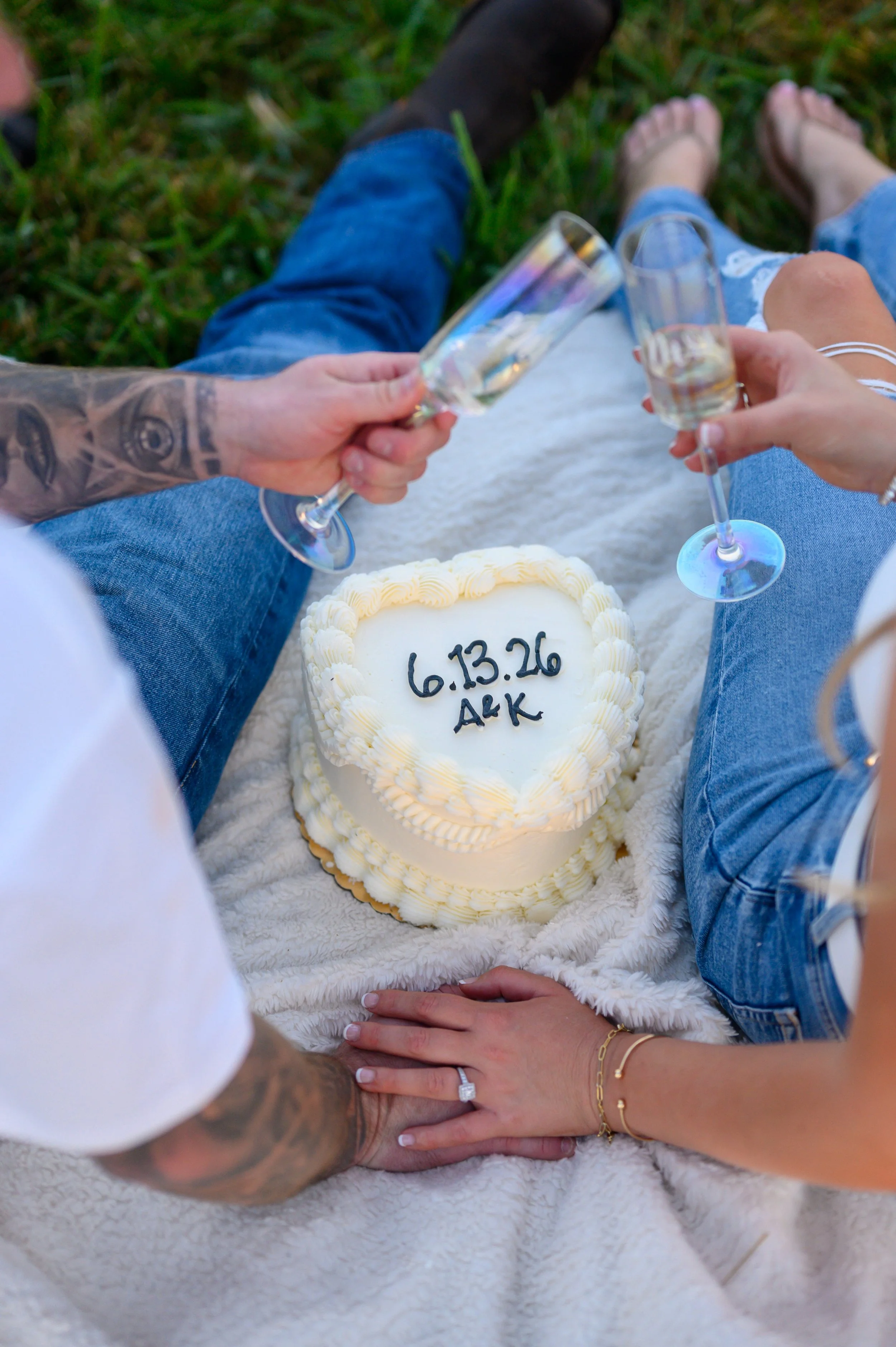 Engaged couple date night having a picnic sharing a cake with the date of their wedding with initials engagement ring showcased sitting on a blanket enjoying the scenery in owensboro Kentucky