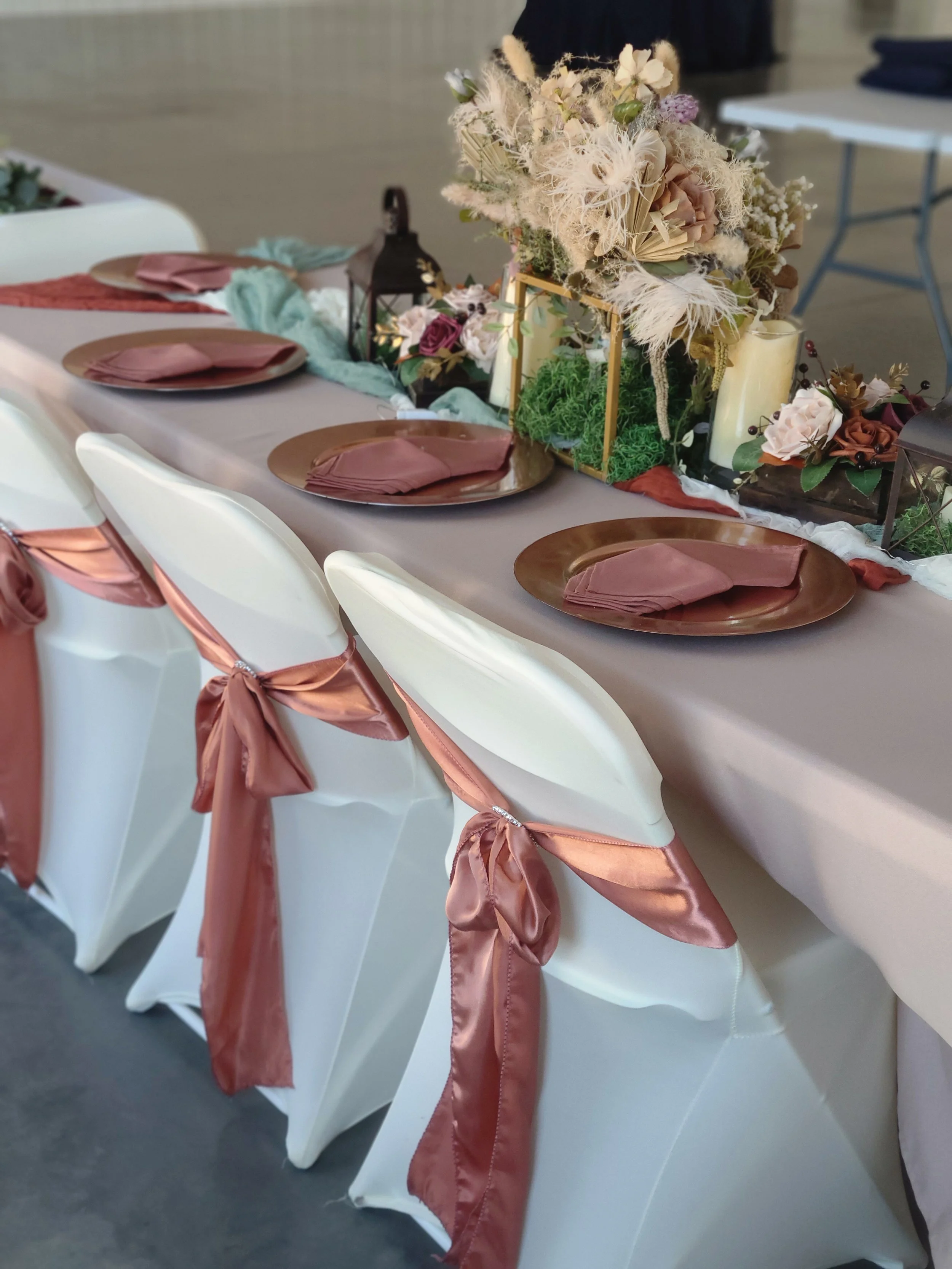 Kentucky Wedding Venue Decor Set up bridal table set rose gold charger plates cream chair covers rose gold chair sashes with diamond rings flameless candles wood frame centerpieces gold centerpiece boho style lantern greenery terracotta table runner