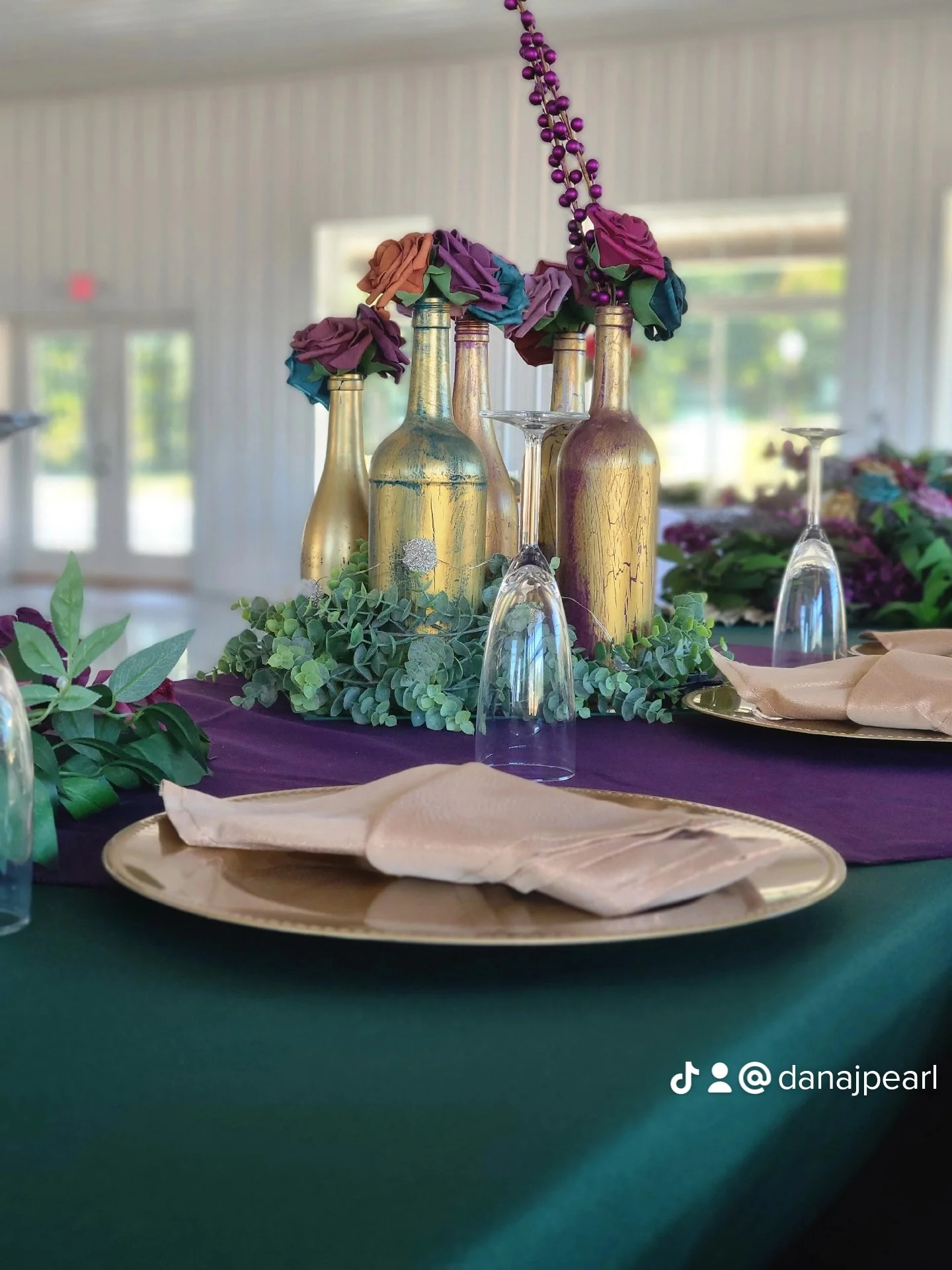 Green tablecloth wine classes gold charger plates gold napkins greenery plum seat covers plum table runner flowers lights and light runners wine bottles bridal table set up decor western kentucky utica owensboro bowling green