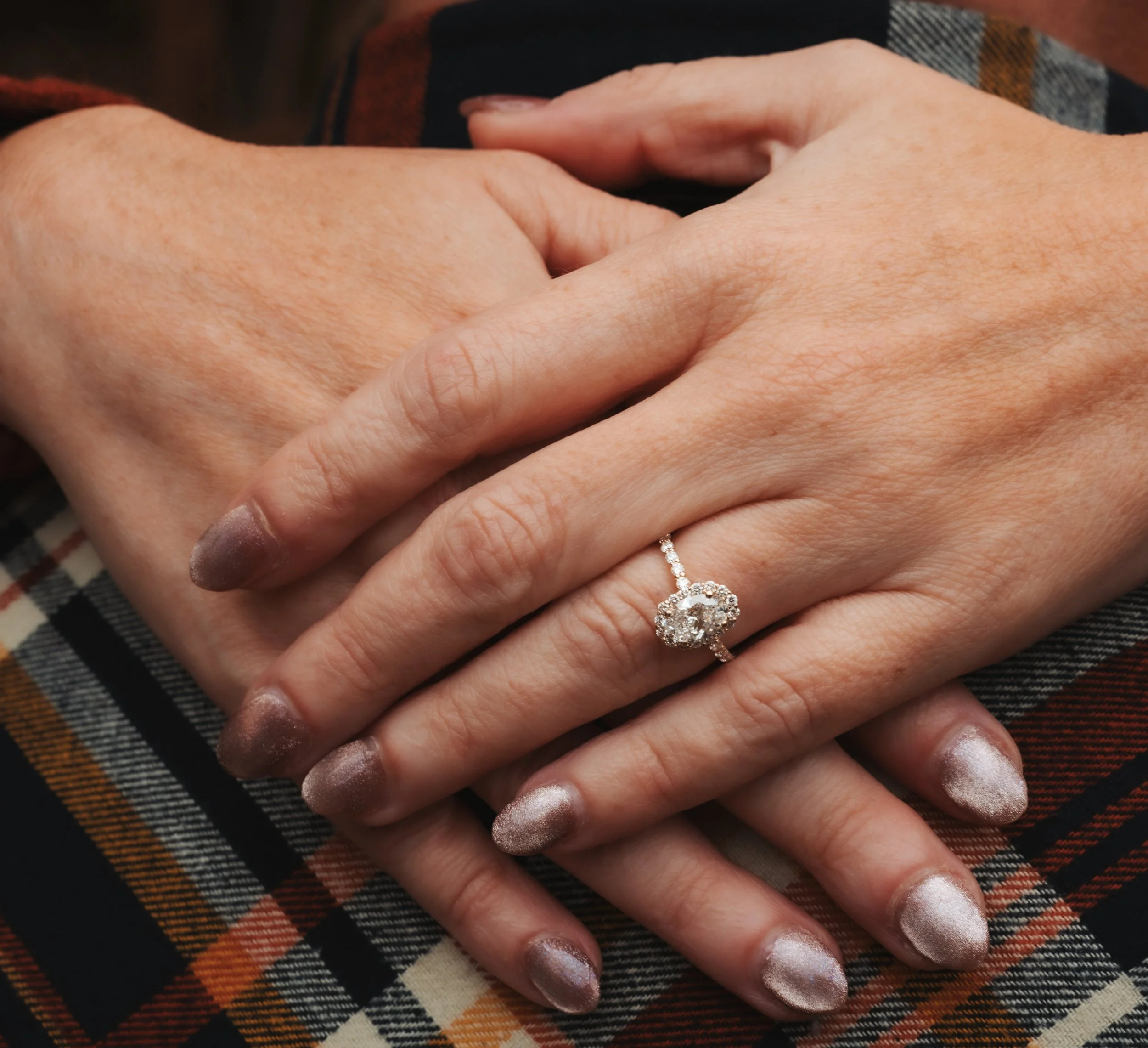 Owensboro Kentucky engaged couple hands overlapping showcasing the engagement ring white gold in color oval shaped diamond cluster diamonds outline flannel shirt for the groom to be glitter painted nails for the bride to be