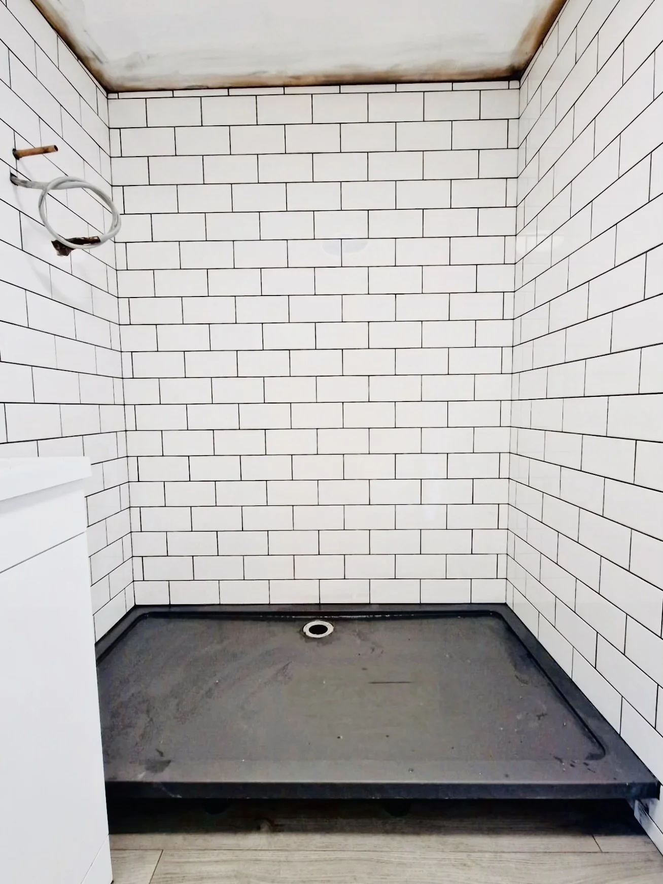 Empty shower stall with white subway tile walls, a circular drain on the floor, and exposed plumbing.