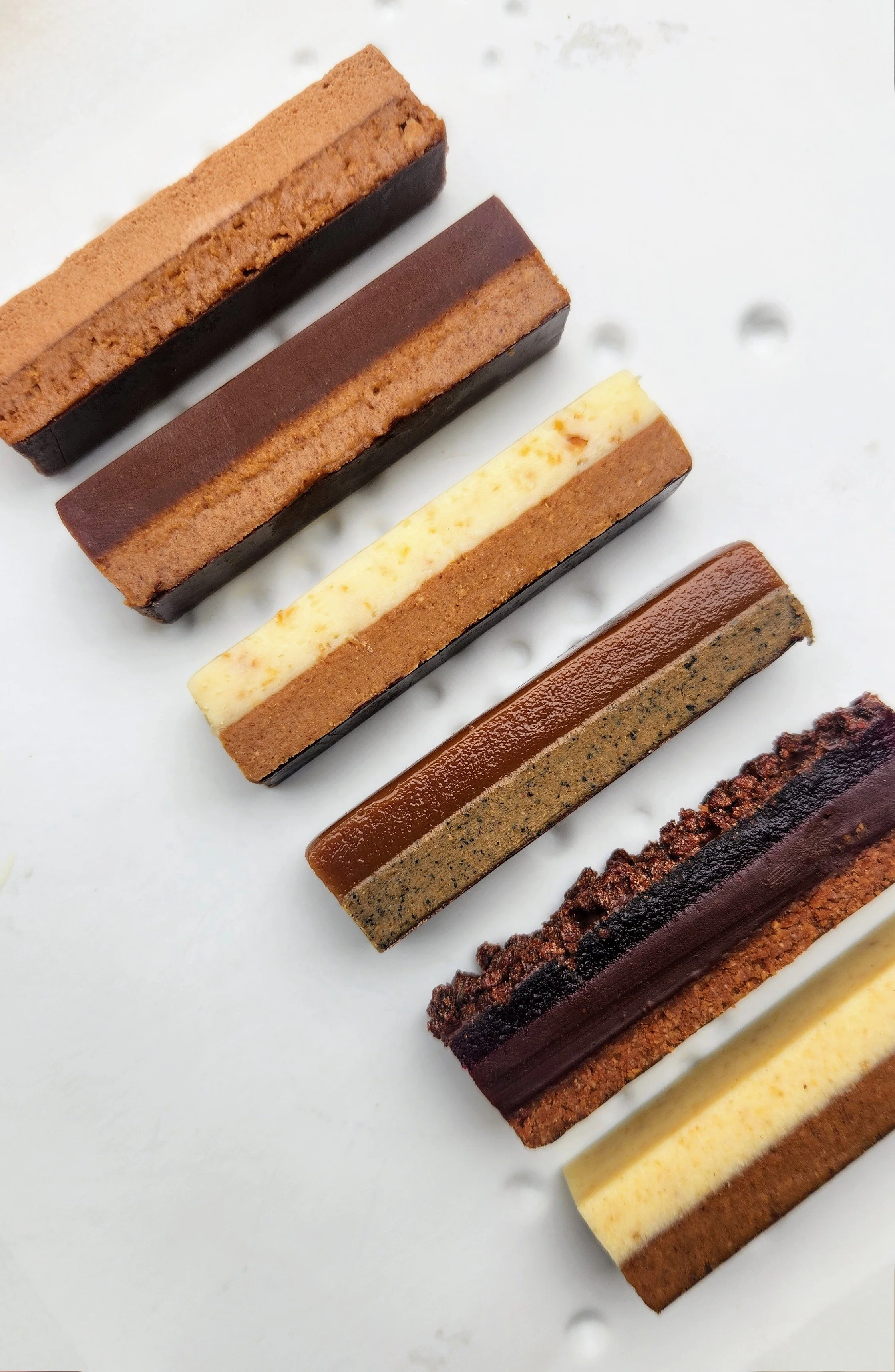 Six assorted layered dessert bars on a white surface.