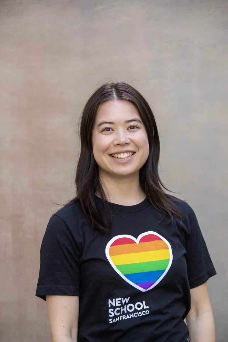Woman smiling, wearing a black T-shirt with a rainbow heart and text that reads "New School San Francisco"