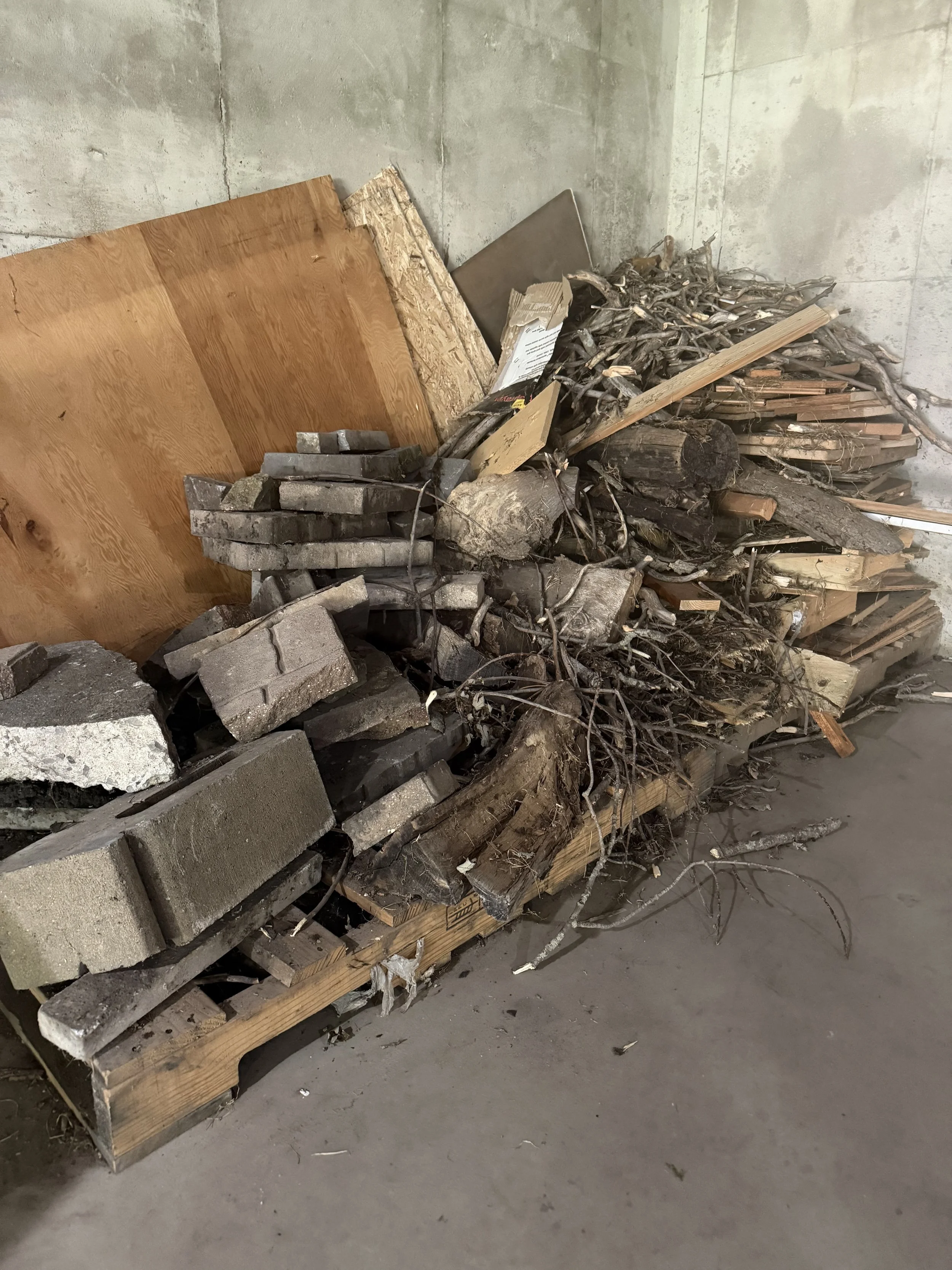 Pallet stacked with construction debris including bricks, wood, and discarded branches, placed against a concrete wall.