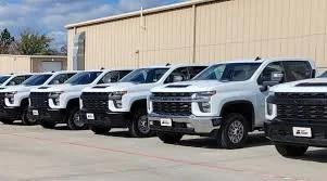 A row of white pickup trucks parked outside a beige industrial building.