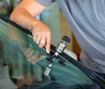 Person using a tool to examine or repair a car's windshield.