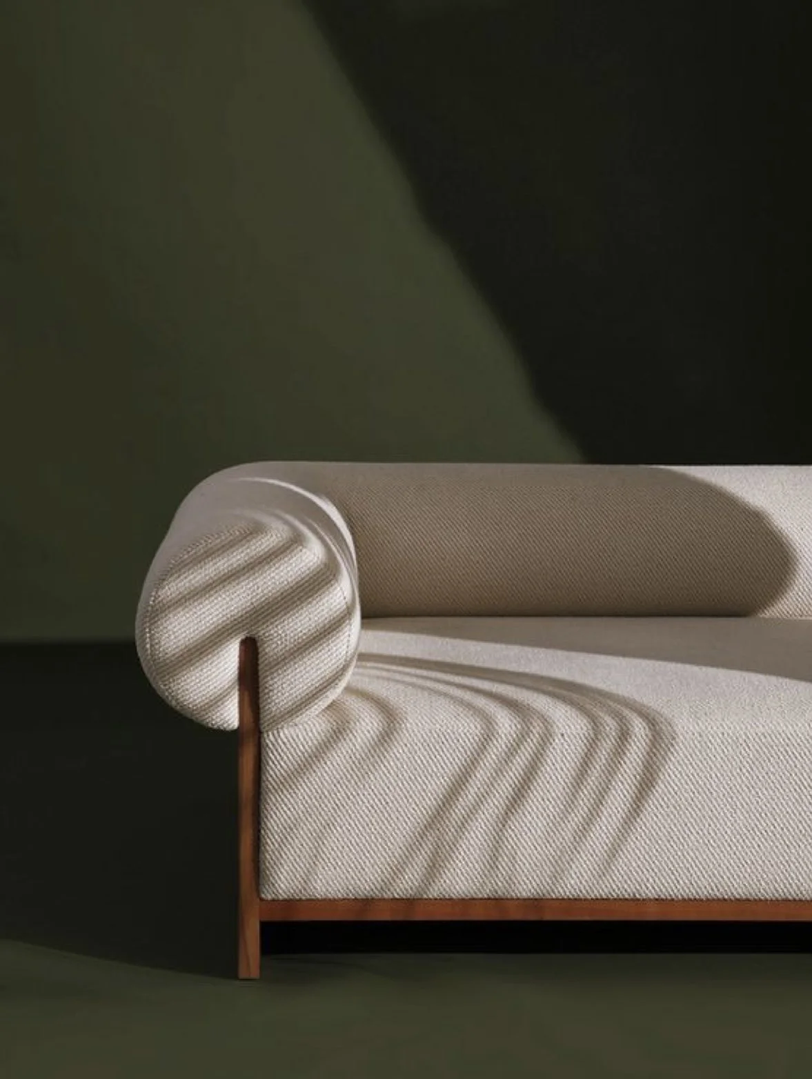 A beige upholstered sofa with a rolled armrest, set against a dark green background.