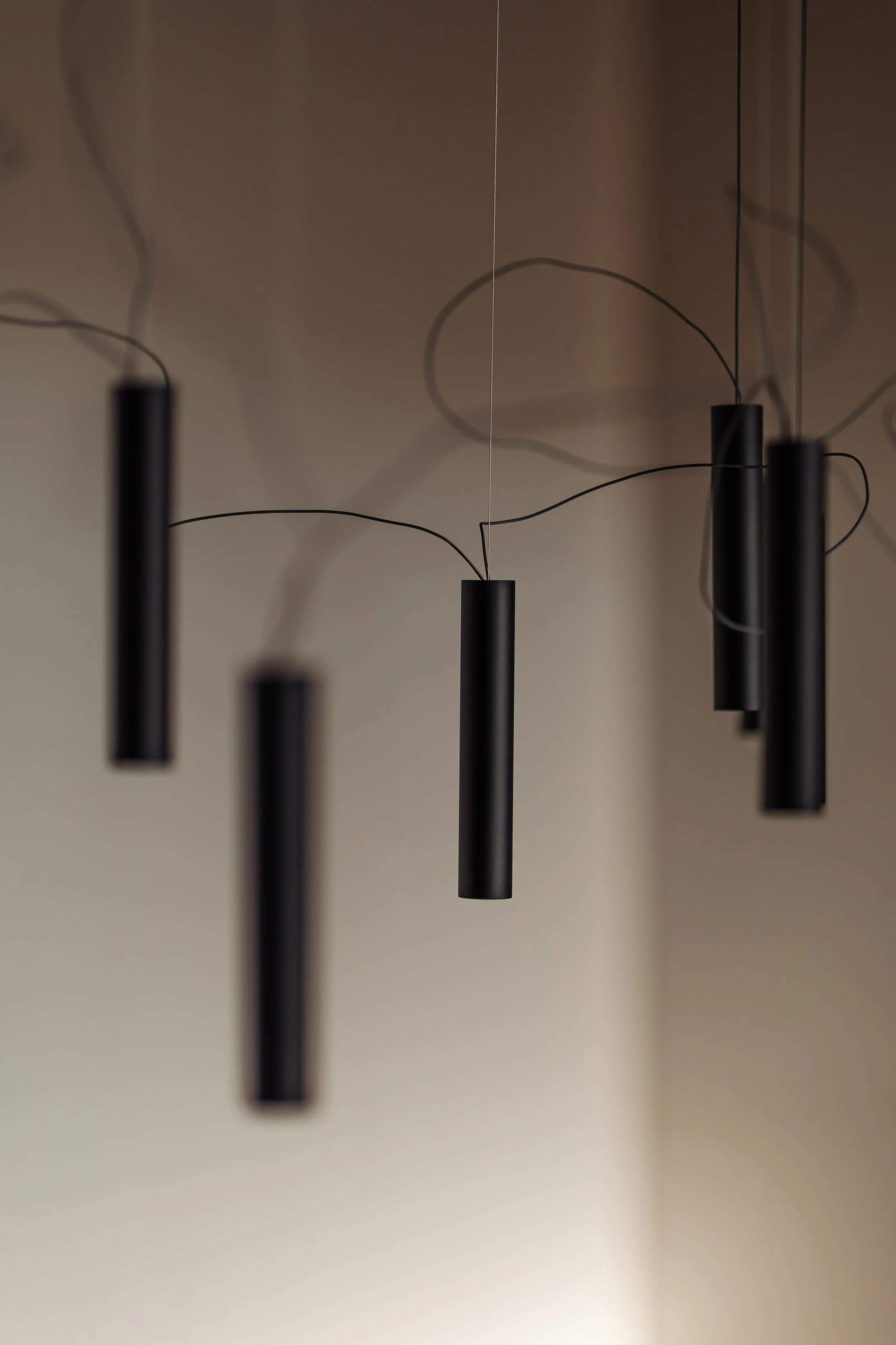 Lustre noir suspendu avec des tiges cylindriques, reflet et ombres sur le mur beige