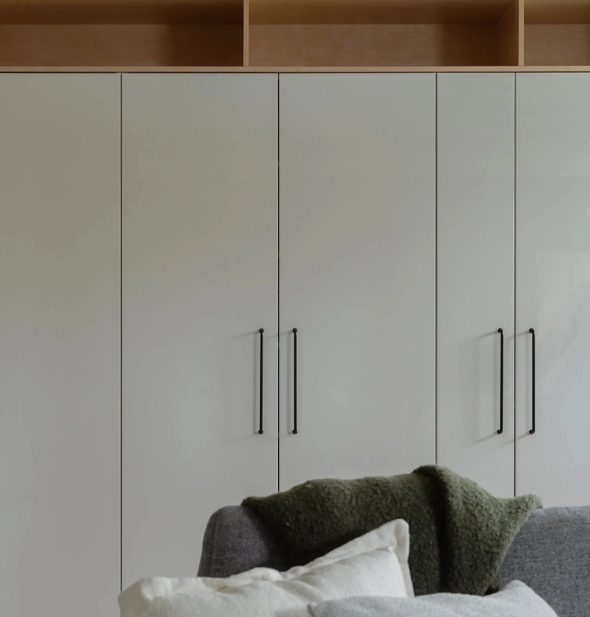 Grand placard blanc avec quatre portes et poignées noires dans une pièce moderne, avec un canapé gris en avant et des coussins blancs et verts.