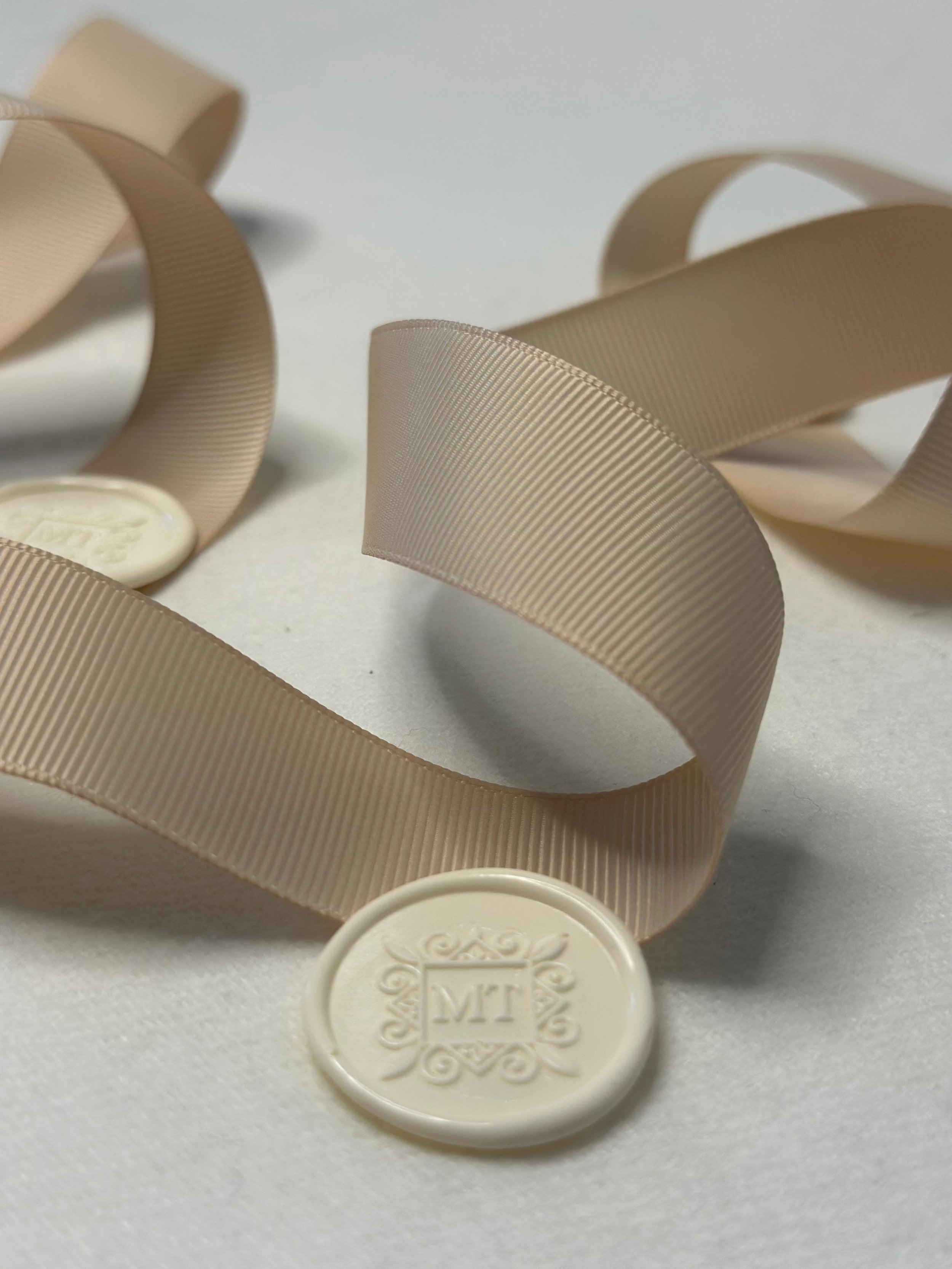 Cream-colored ribbon and wax seal with initials 'MT' on a white surface.