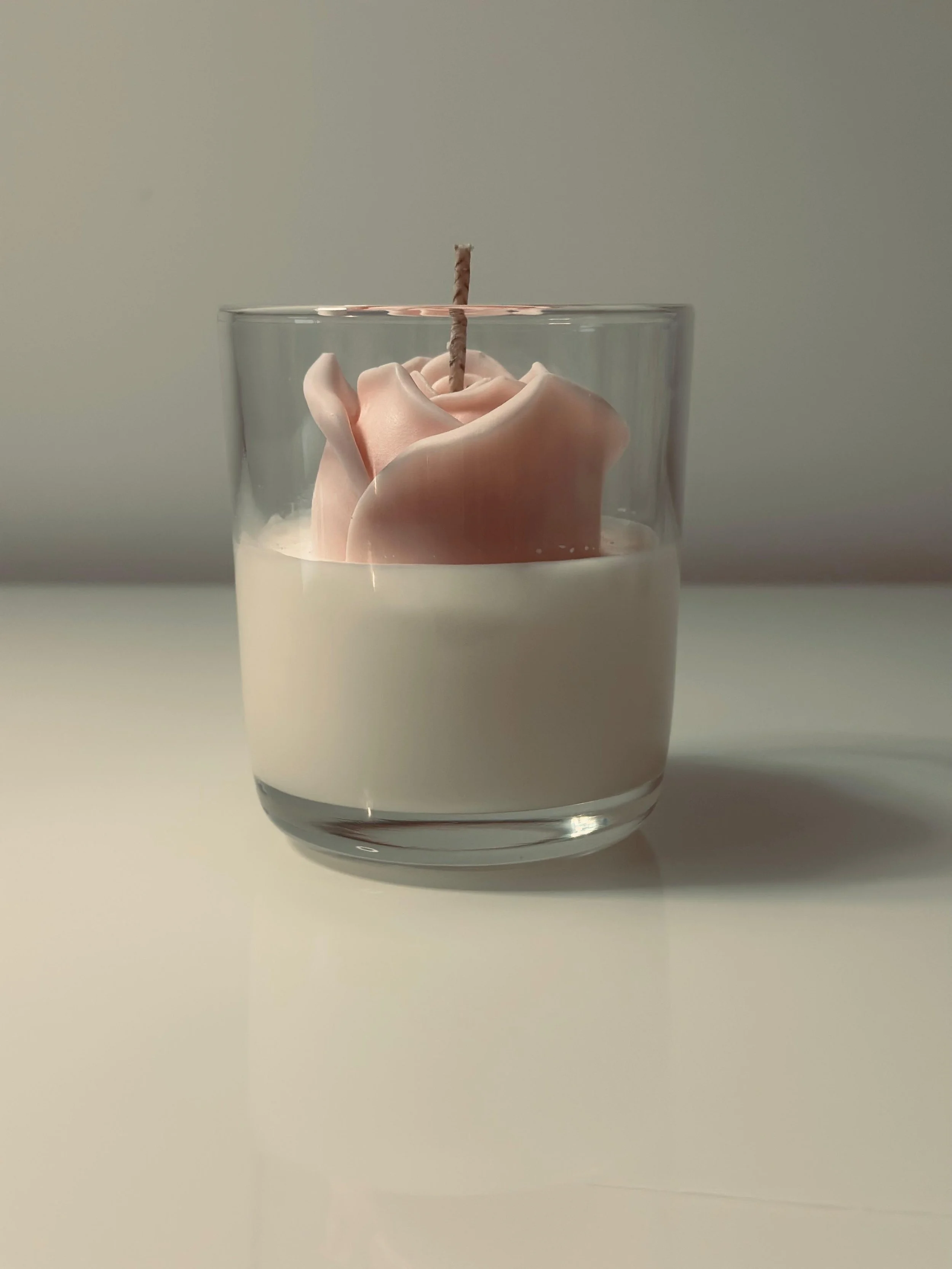 Candle in a glass holder with a pink flower-shaped wax sculpture and a wick on top