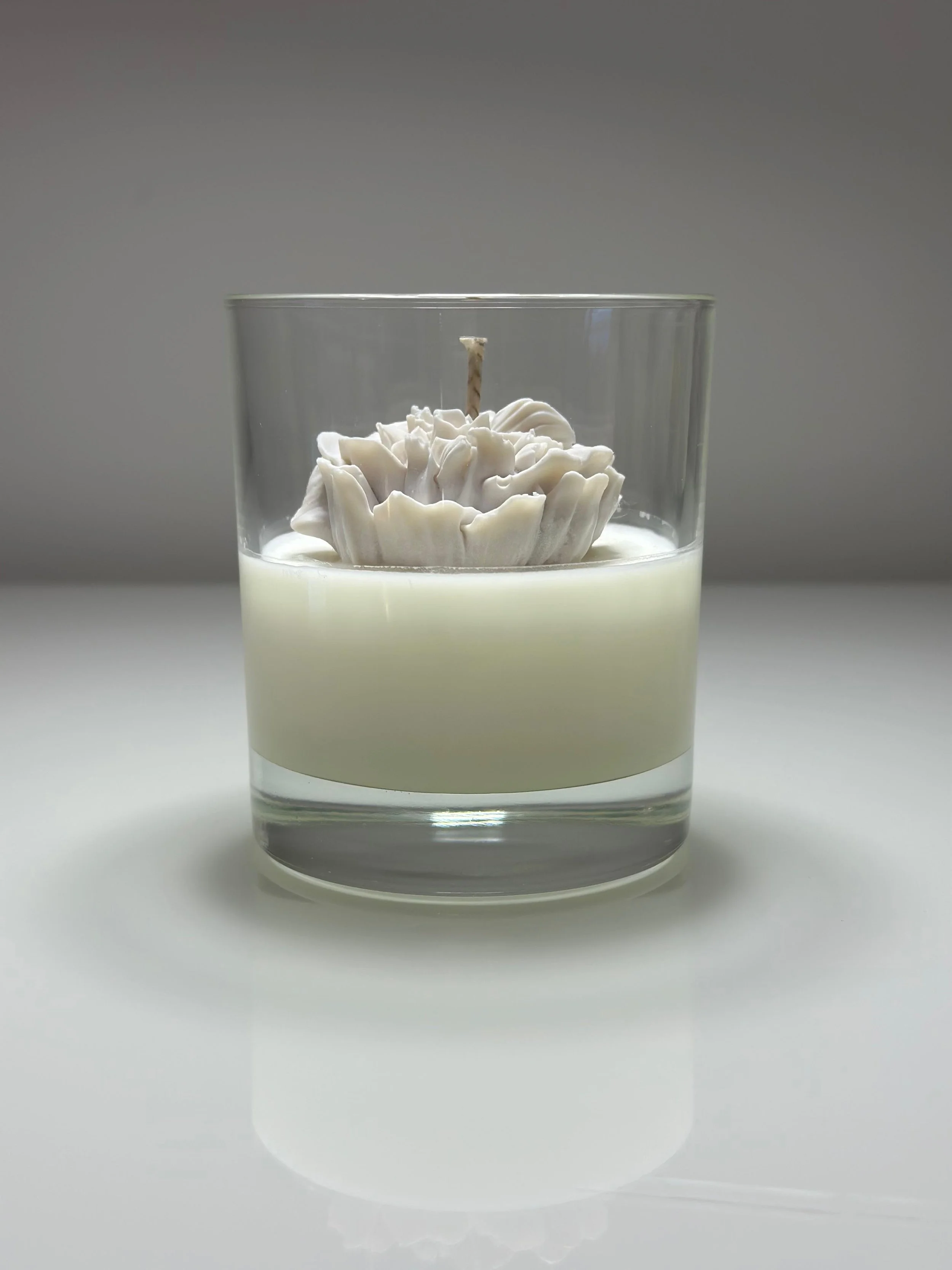 White candle with a decorative flower design in a clear glass container filled with white wax