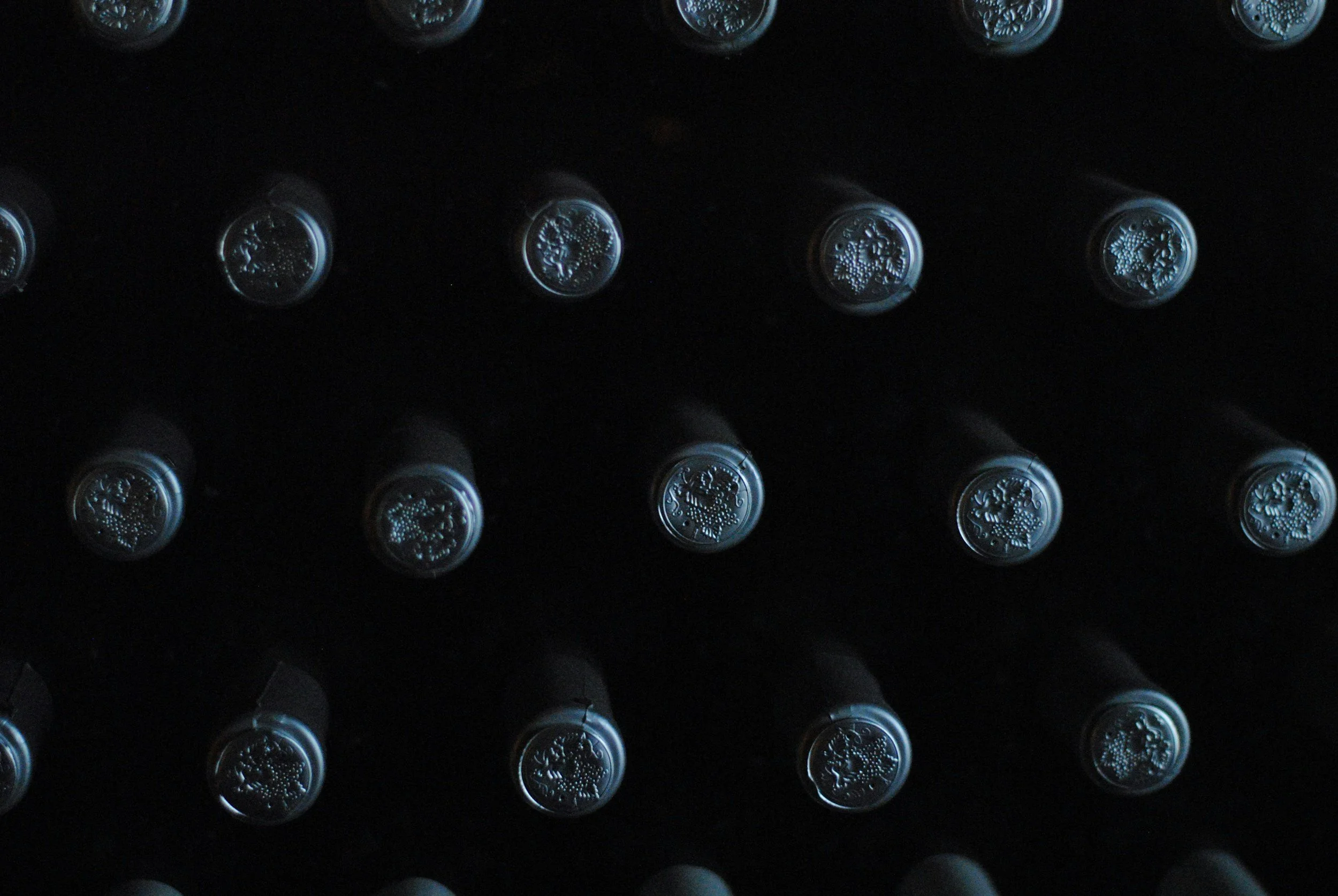 A grid of wine bottles stored horizontally in a dark wine cellar or storage area.
