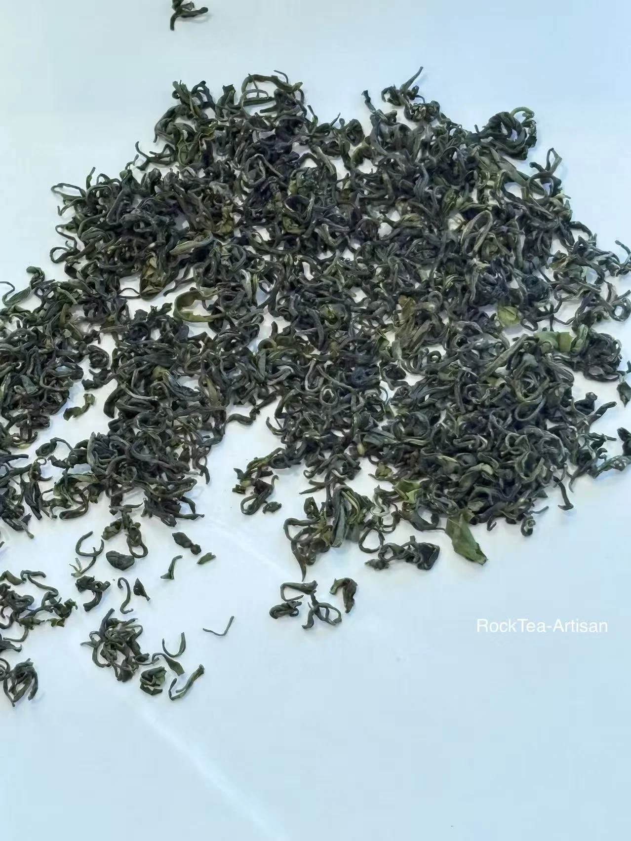 Close‑up macro shot of dry Taishan Daughter Tea, a current‑harvest northern‑Chinese wok‑fired green tea. Tightly curled deep‑green leaves, characteristic chestnut‑aroma spring green tea in Montreal.