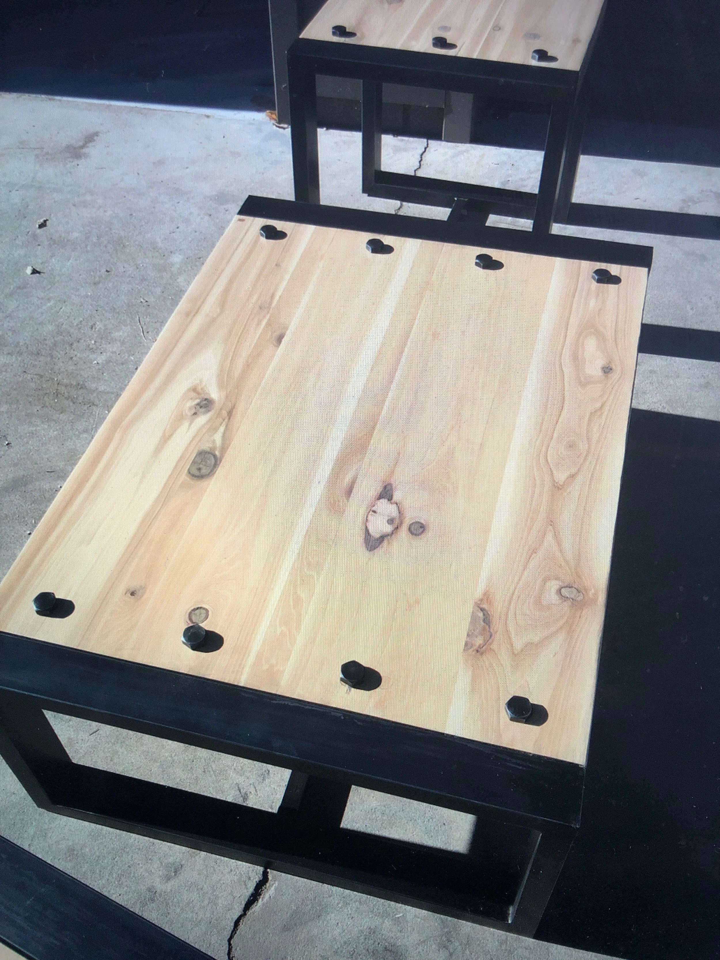 A shuffleboard table with a wooden playing surface and black frame, placed outdoors on a concrete surface.