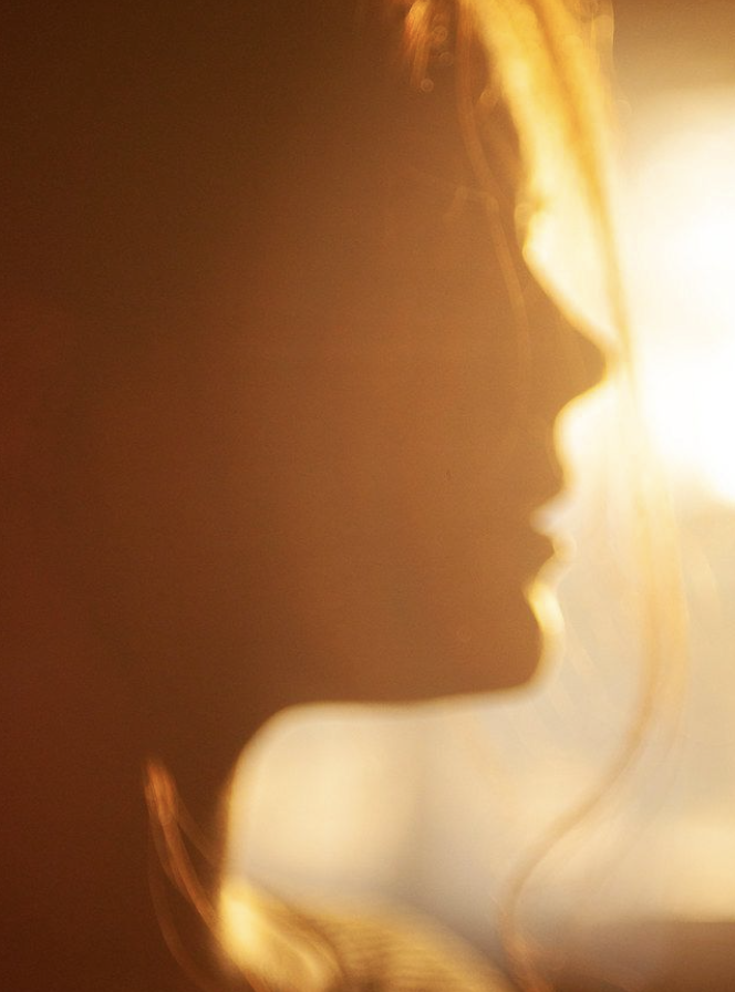 Silhouette of a young woman in profile with sunlight illuminating her from behind.