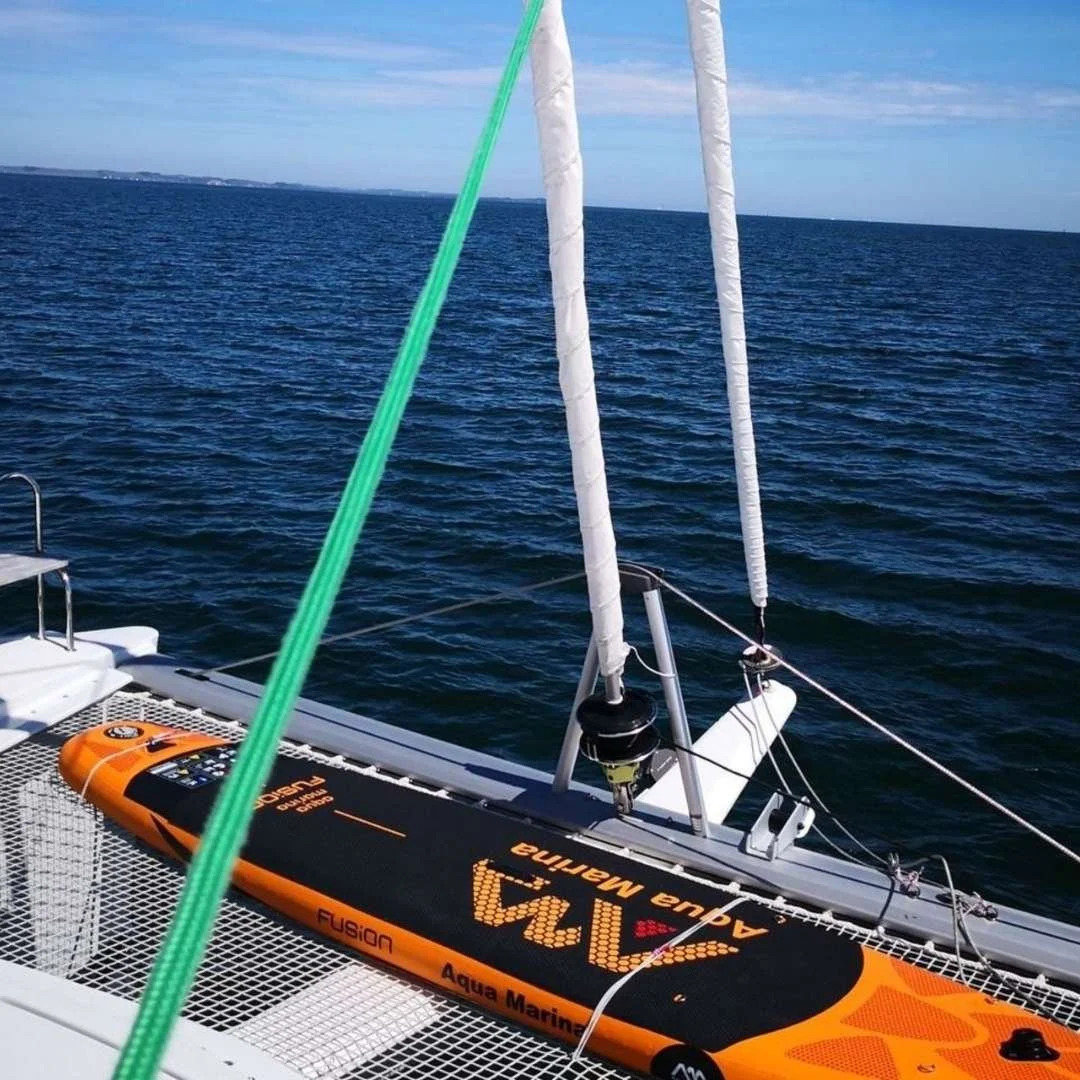 Orangefarbenes Aqua Marina Fusion SUP Board auf dem Trampolin des Segelkatamarans von Baltic Sea Yacht Events