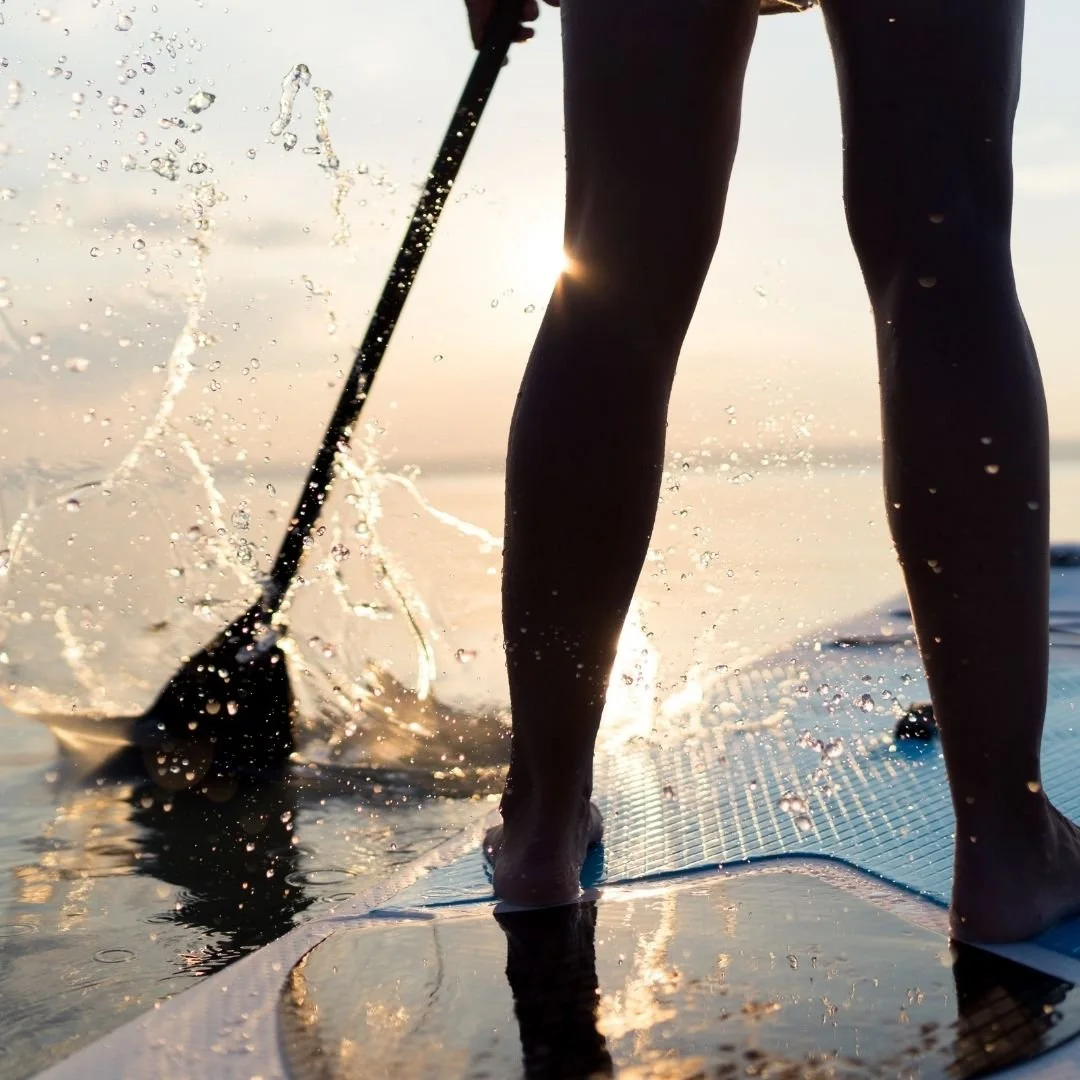 Nahaufnahme Stand Up Paddling bei Sonnenuntergang - Füße auf SUP Board mit Wasserspritzern auf