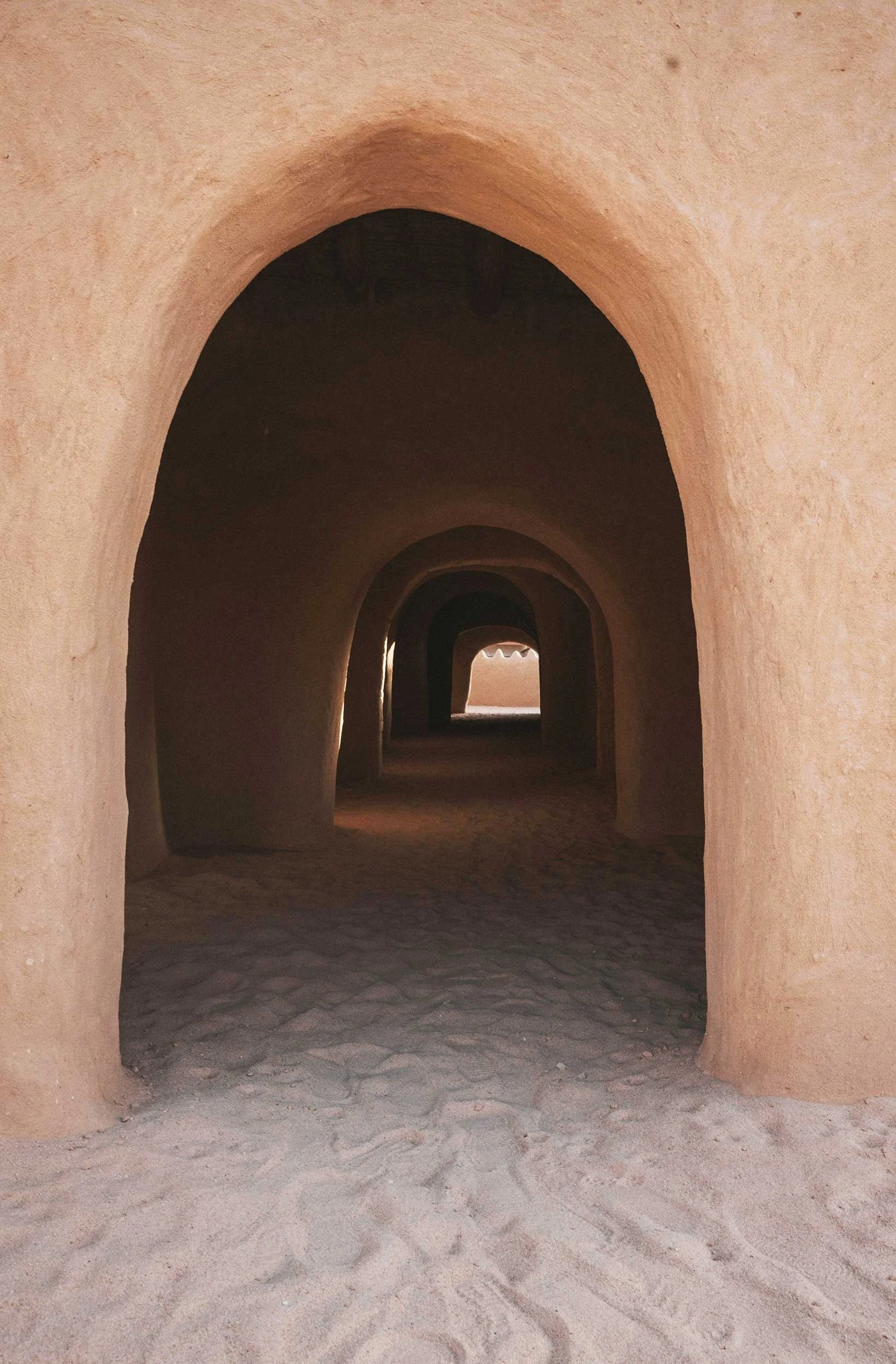 Series of arched passageways creating a tunnel with sand on the ground.