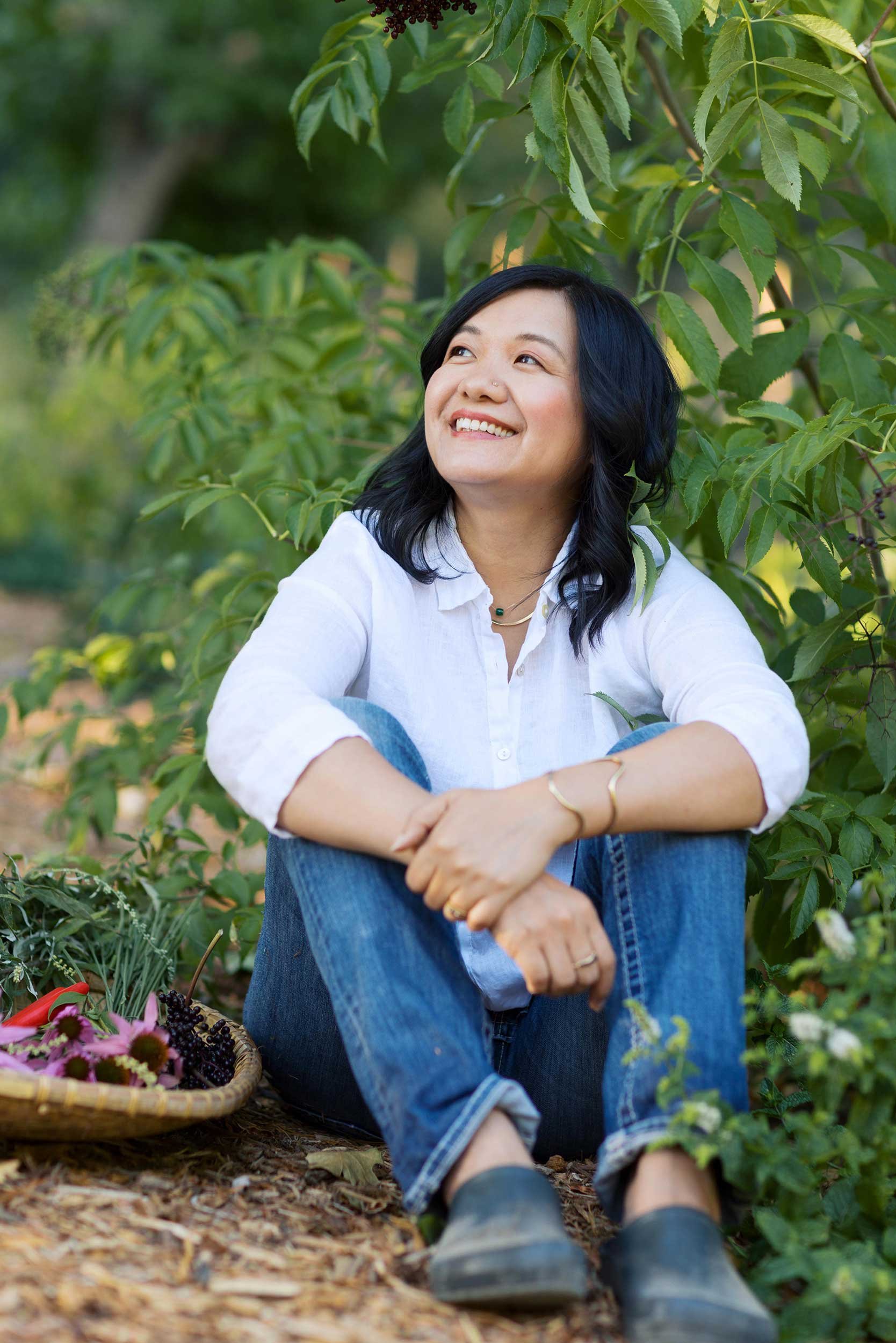 Woman sitting outdoors in greenery looking upward in a moment of reflection and connection with nature.