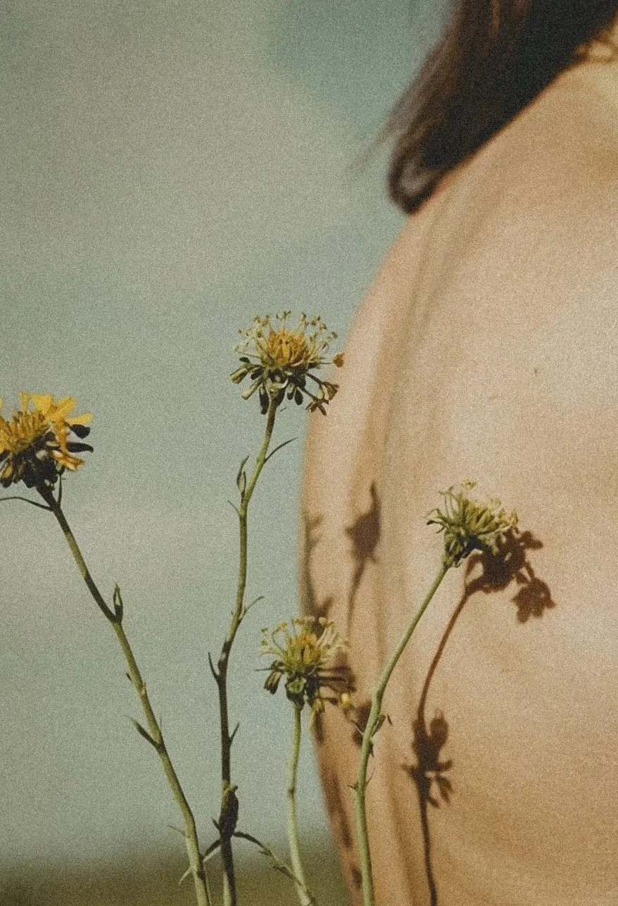 Dried wildflowers placed near a person’s shoulder in soft natural light.