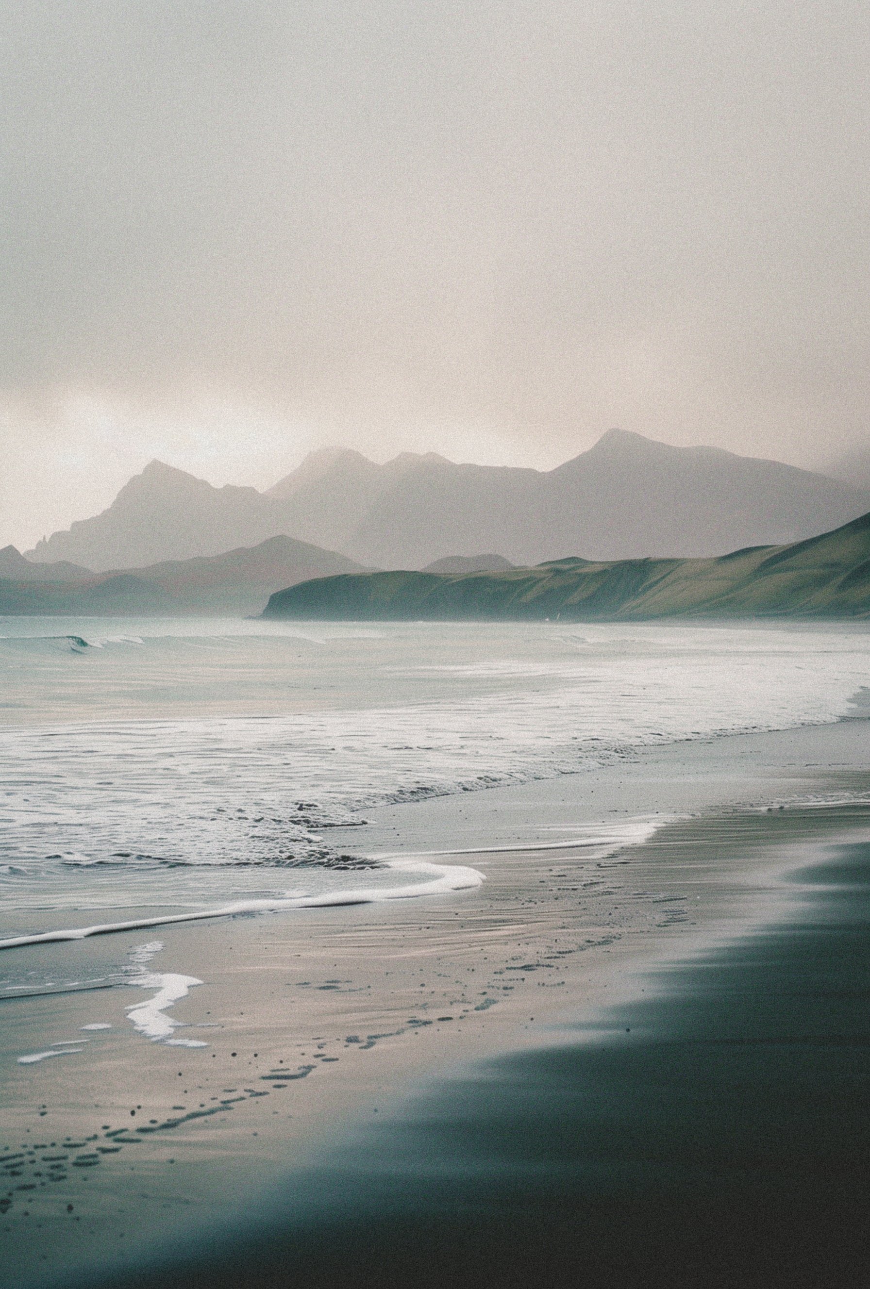 Beach shoreline with mountains in the distance and waves along the coast.